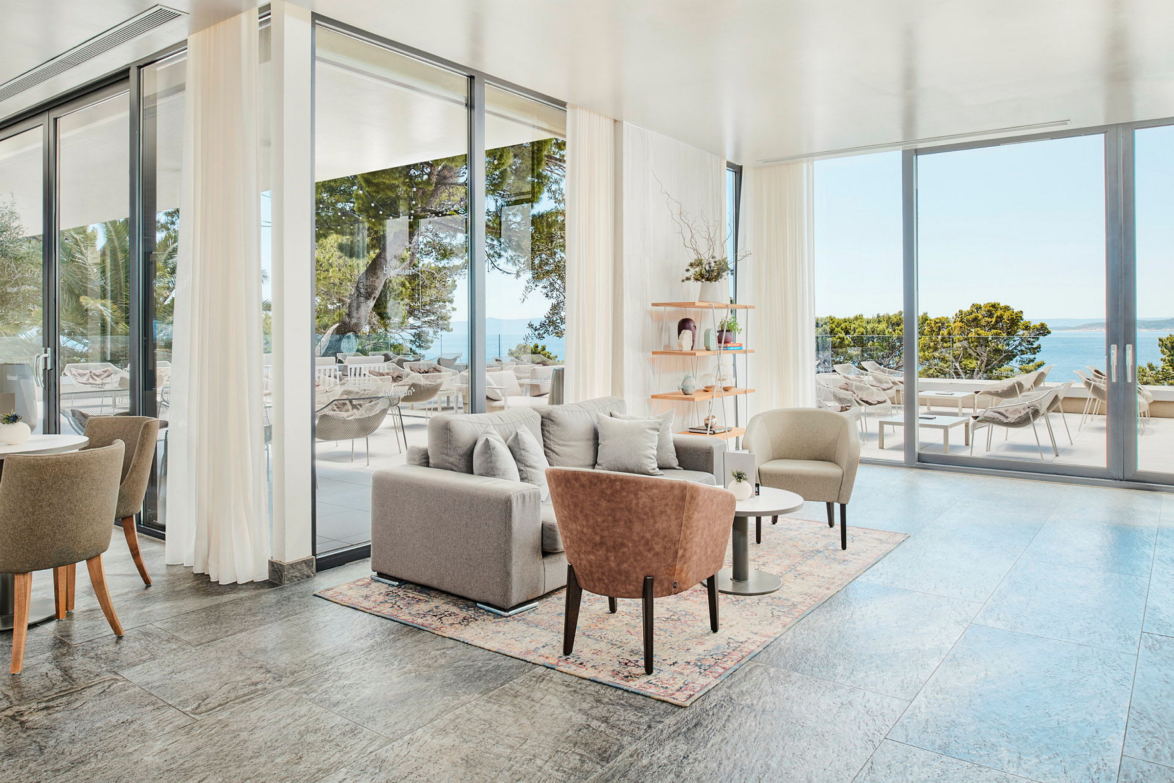 Et moderne og lyst oppholdsrom med glassdører som fører ut til en terrasse med utsikt over havet. (AI-generert tekst)