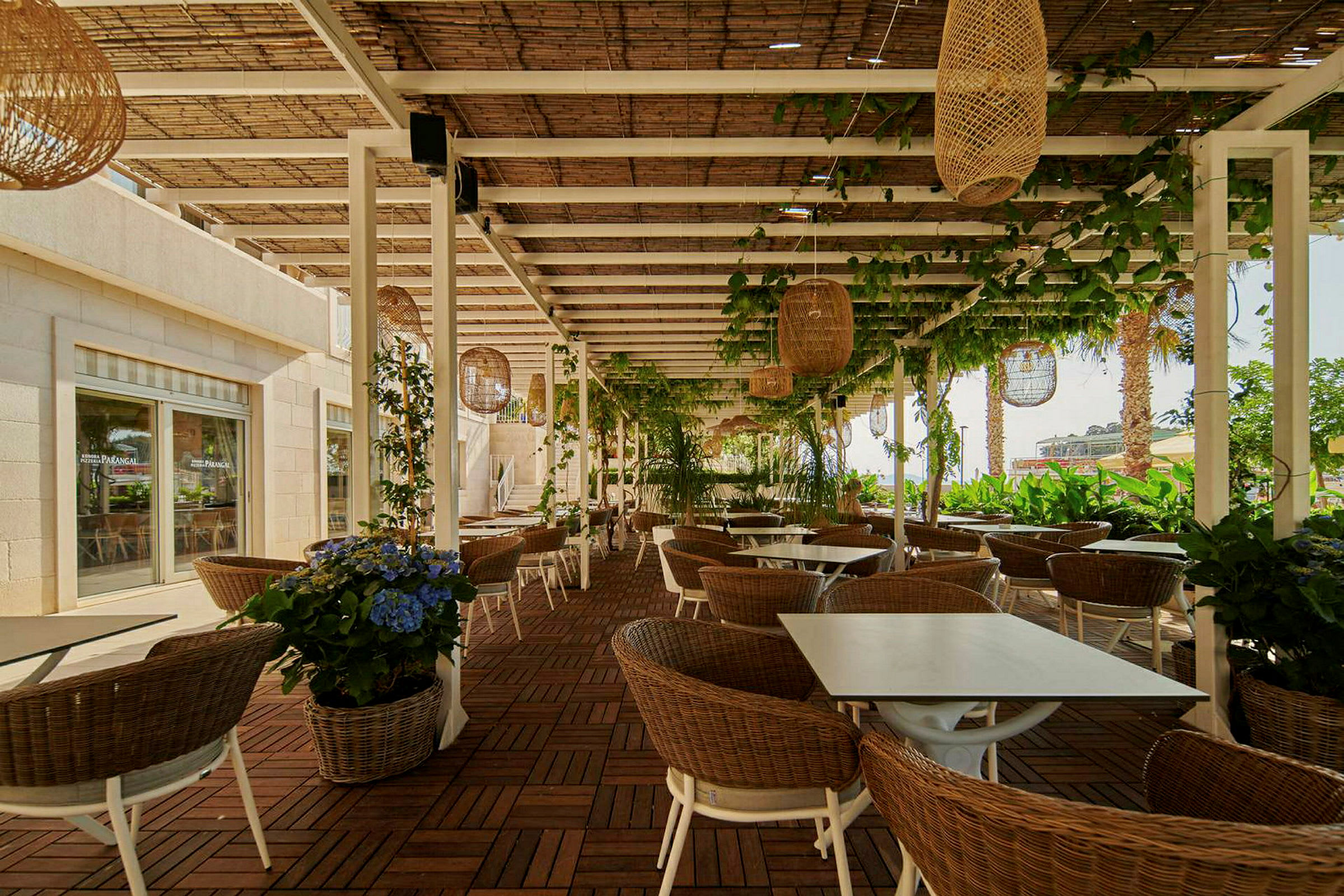 Uteservering med bord, stoler og planter under en pergola. (AI-generert tekst)