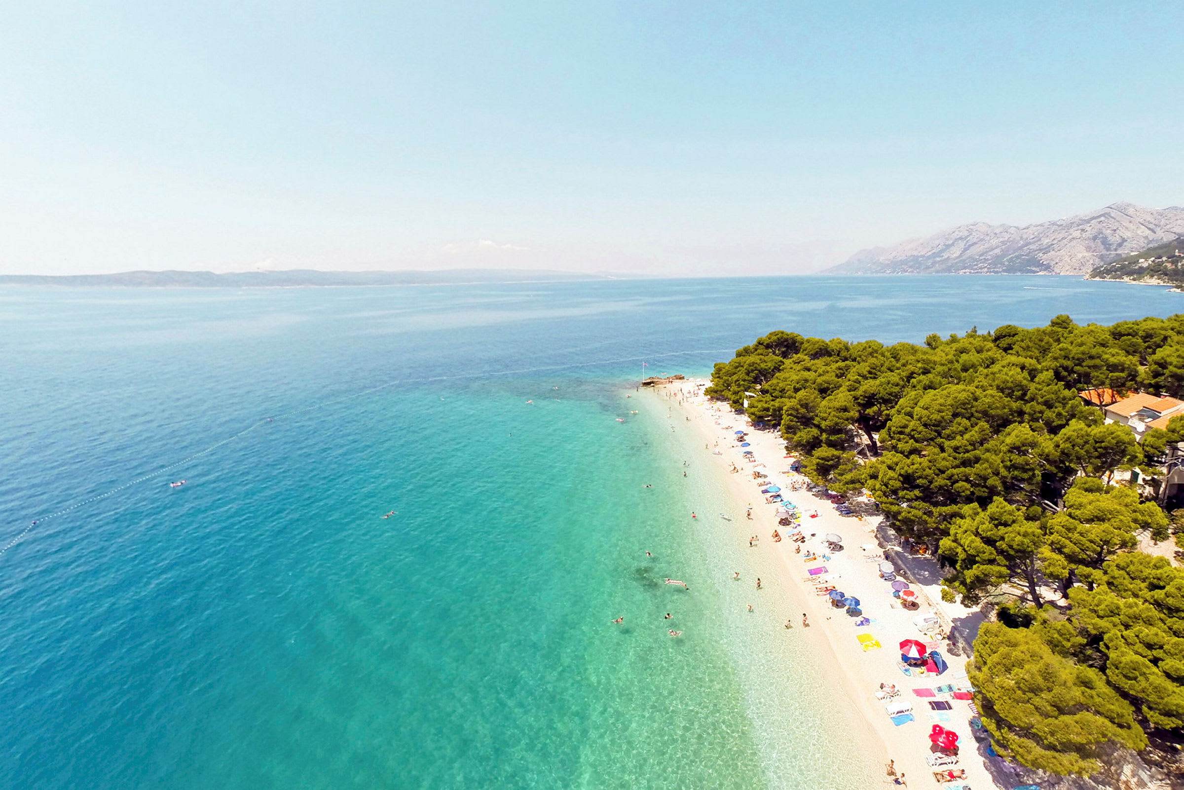 Hvit sandstrand med turkis hav og omkransende grøntområder. (AI-generert tekst)