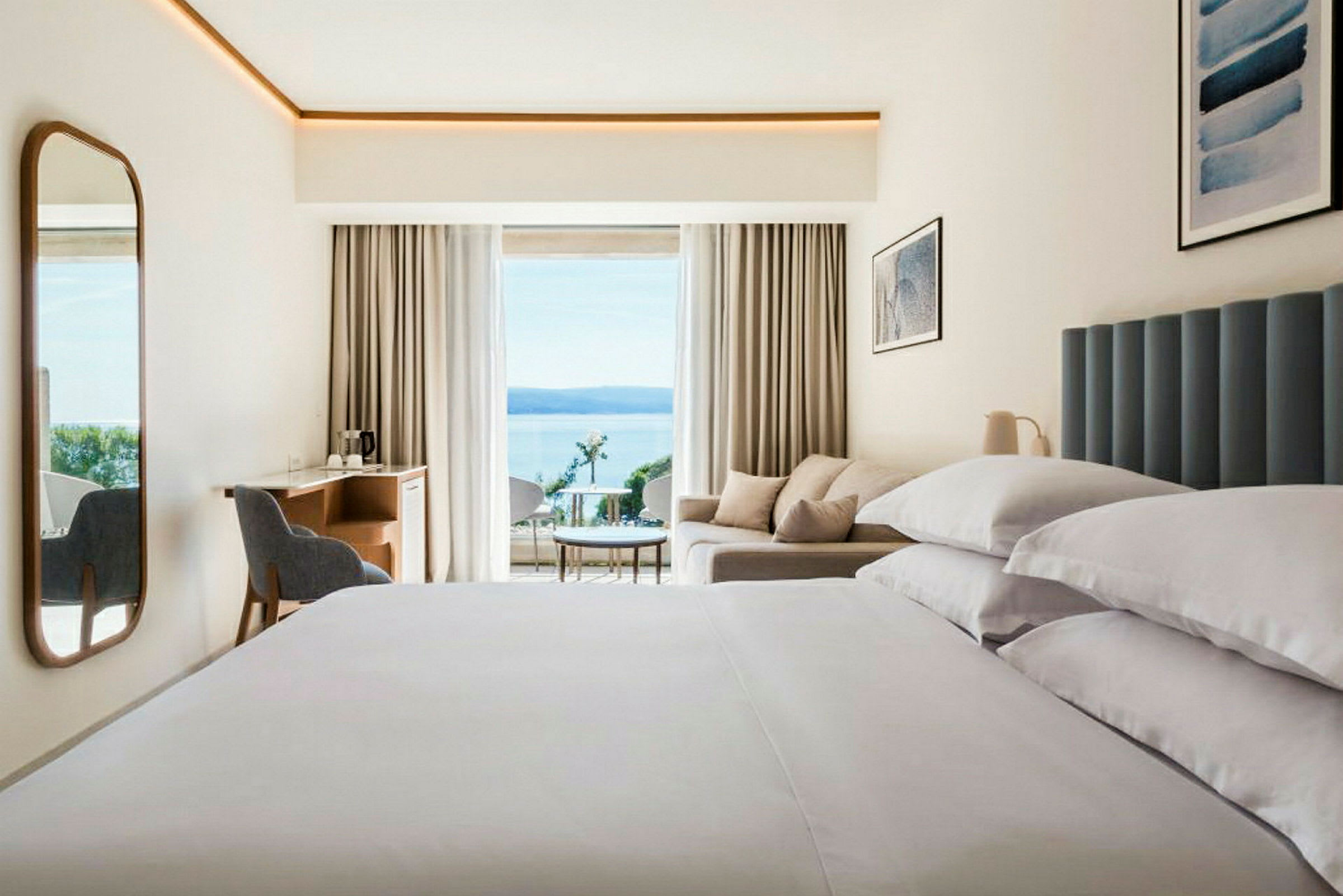 Moderne hotellrom med stor seng, sofa og havutsikt. (AI-generert tekst)