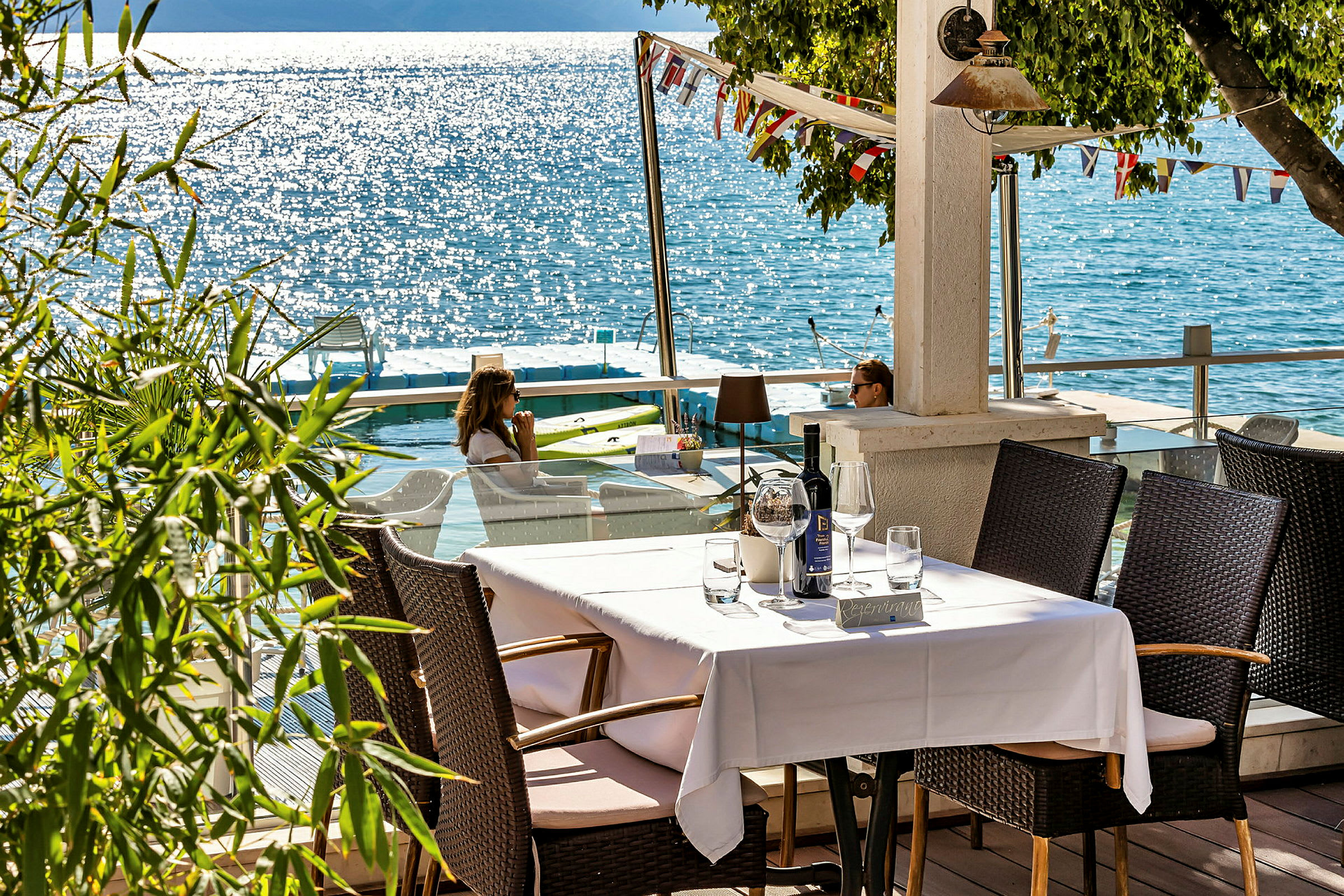 Et dekket bord på en terrasse med utsikt over en solglitrende innsjø. (AI-generert tekst)