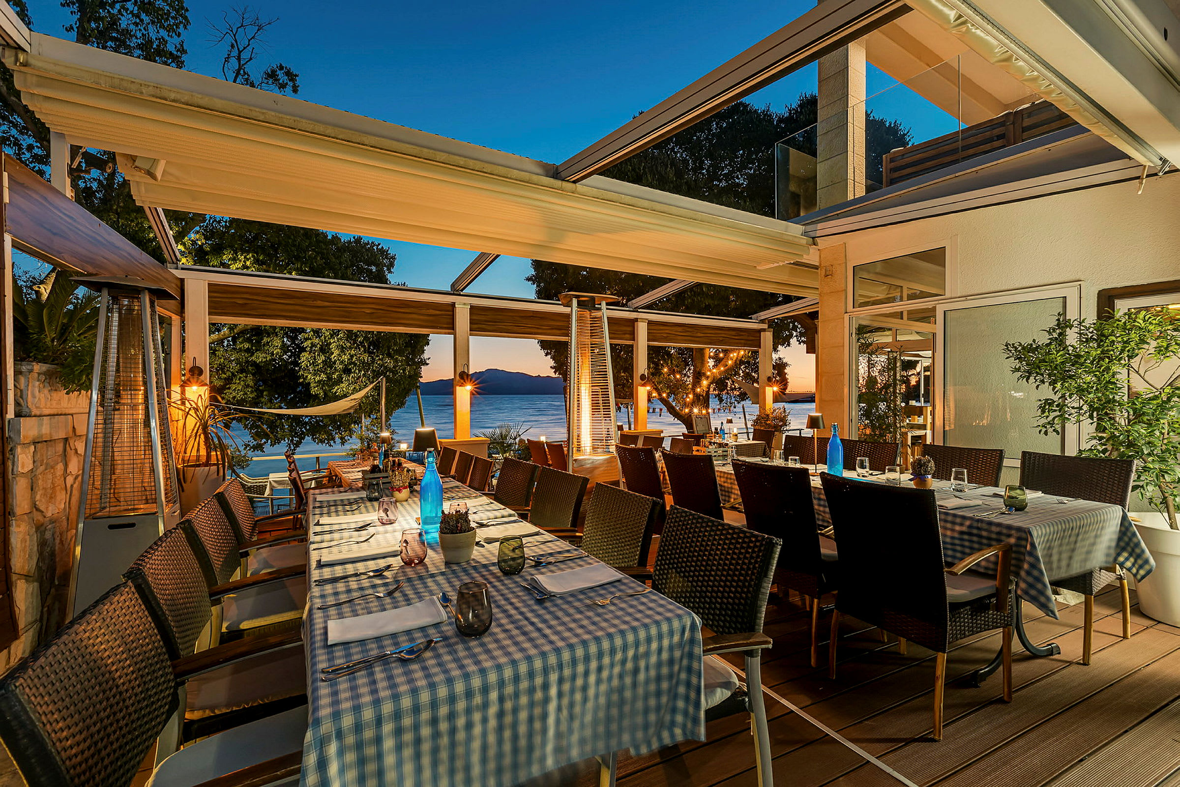 Bilde av en utendørsrestaurant med dekket bord og utsikt mot sjøen. (AI-generert tekst)