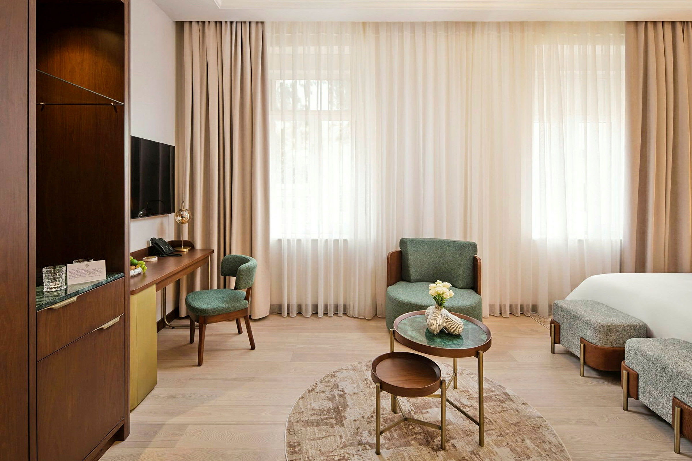 Et lyst hotellrom med moderne møbler, et skrivebord med stoler og et lite salongbord med dekorative blomster. (AI-generert tekst)