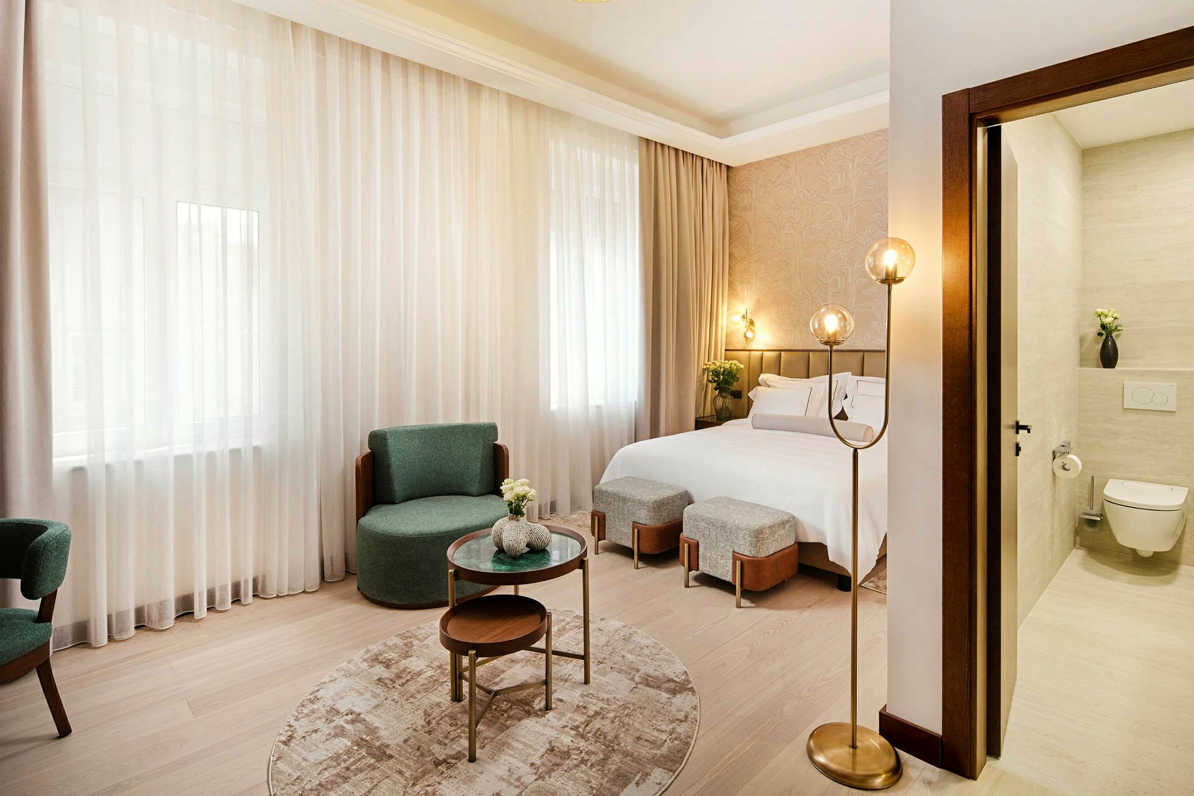 Et moderne hotellrom med dobbeltseng, stoler, sofabord og en delvis synlig baderomsdel. (AI-generert tekst)