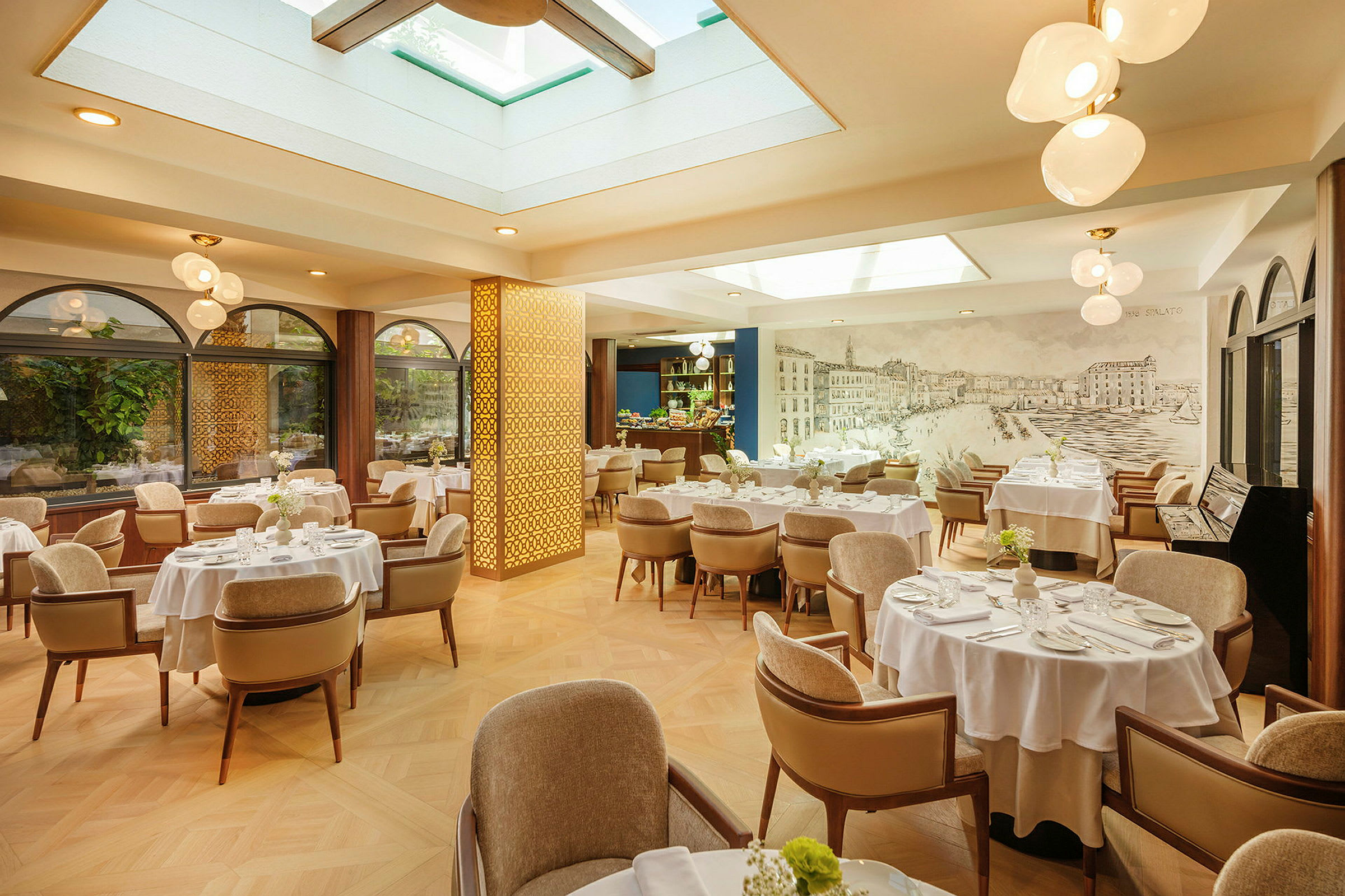 En lys og elegant restaurant med bord med hvite duker og komfortable stoler. Vinduer med planter utenfor og takvinduer gir naturlig lys. (AI-generert tekst)