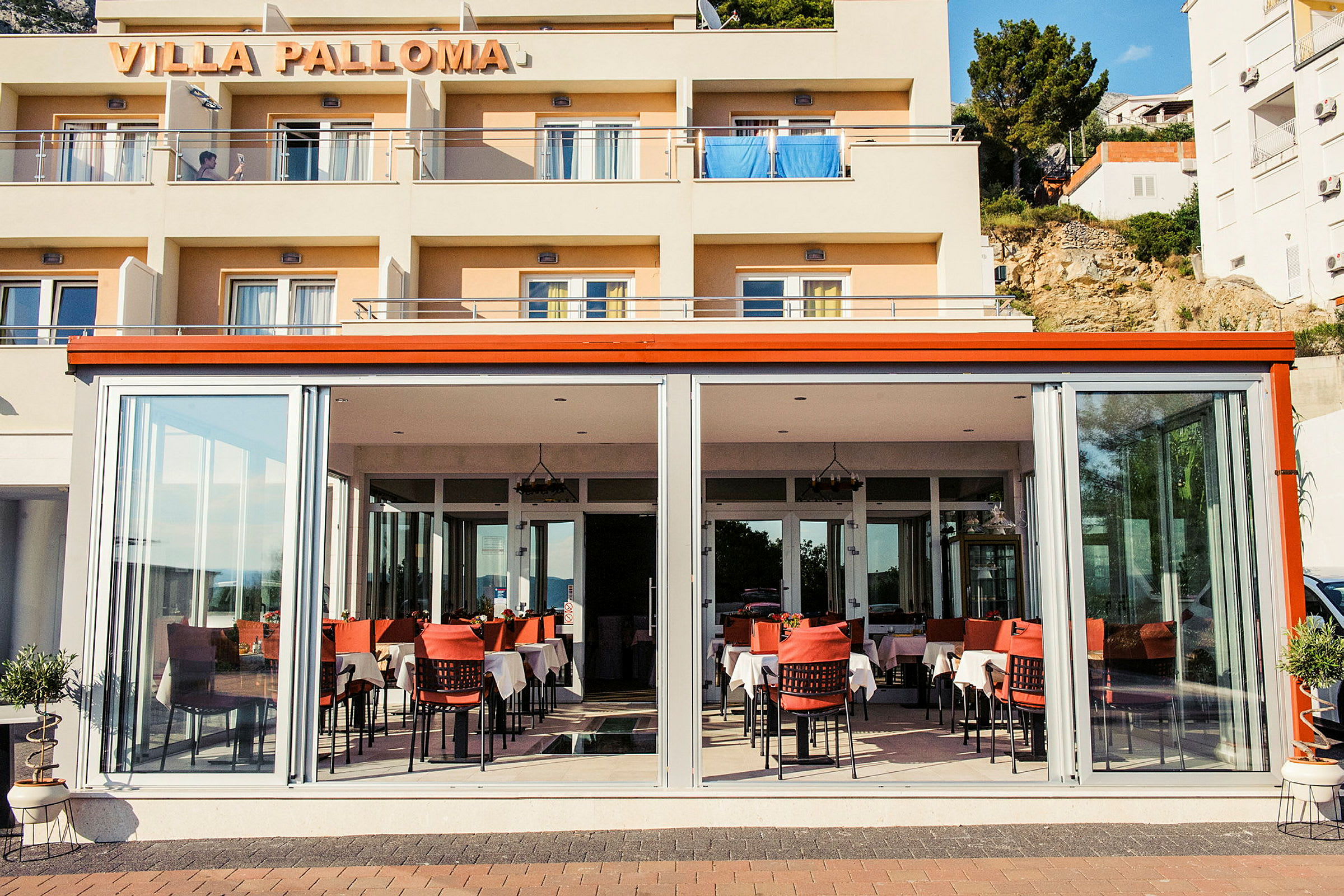 Inngangen til Villa Palloma med en restaurant fylt med dekte bord. (AI-generert tekst)
