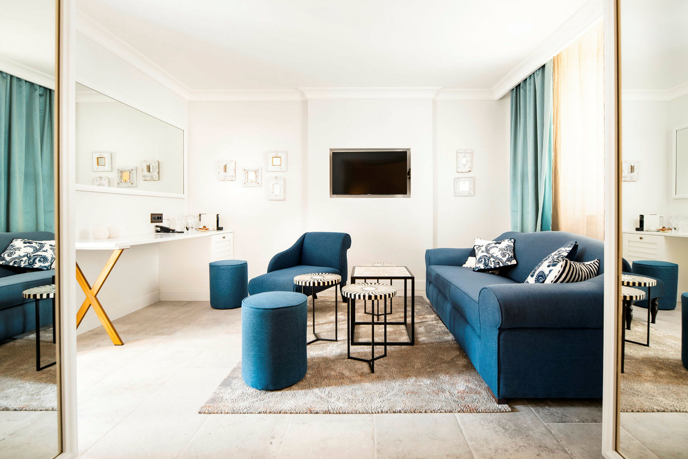 En moderne innredet stue med blå sofaer og sittepuffer, et lite bord og en veggmontert TV. (AI-generert tekst)