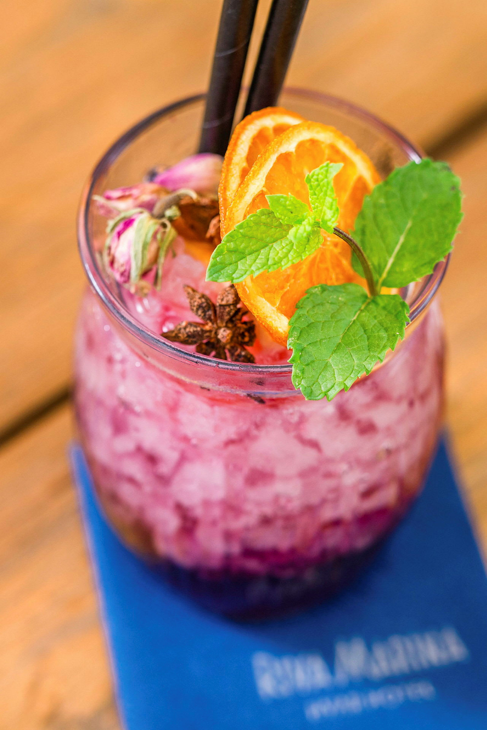 Et glass med rosa knust is og dekorasjoner av appelsinskiver, mynte og krydder. (AI-generert tekst)