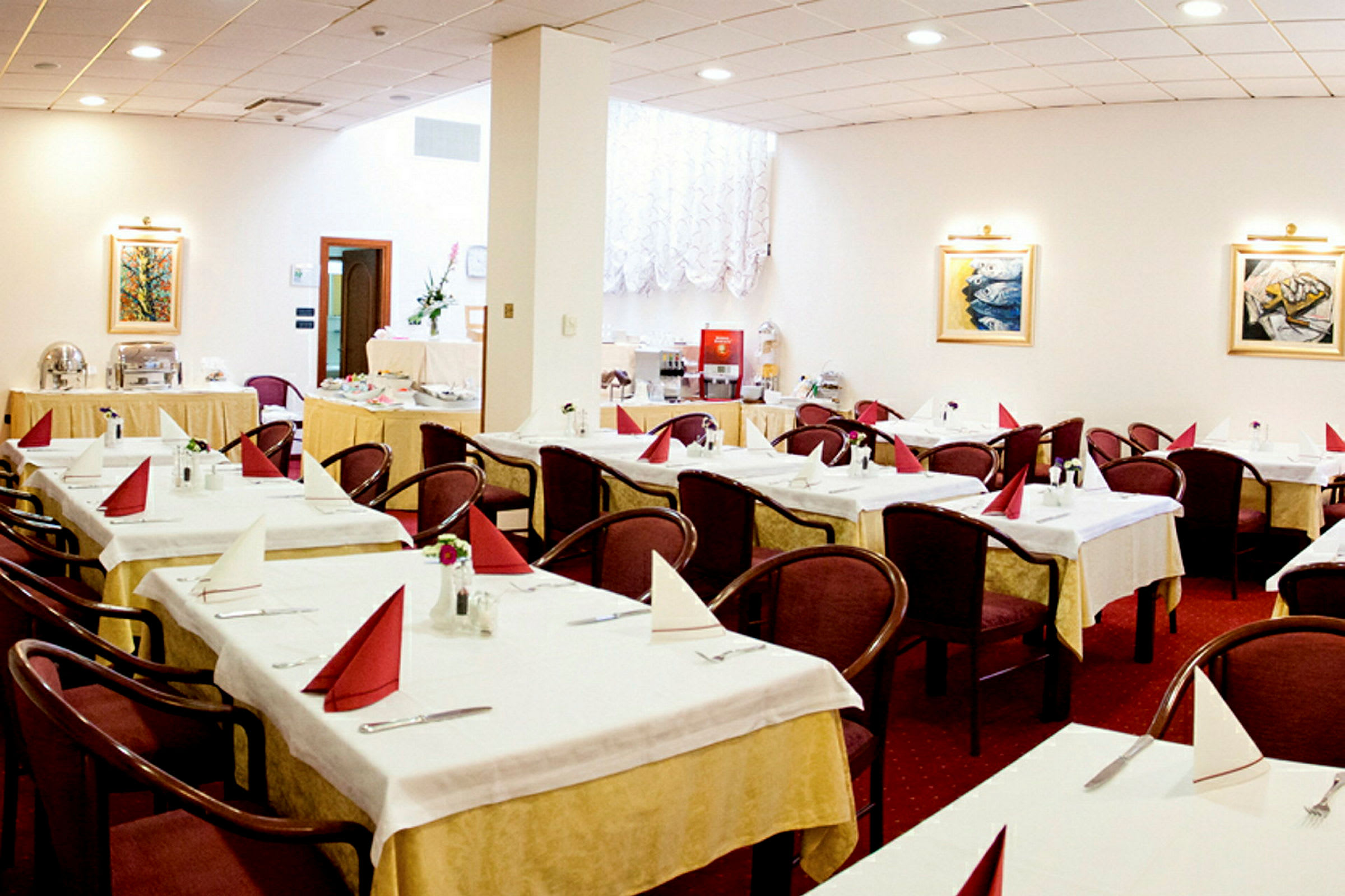 En restaurantinnredning med flere oppstilte bord, hver utstyrt med brettede servietter og stoler, samt dekorasjoner som malerier og vegglamper. (AI-generert tekst)