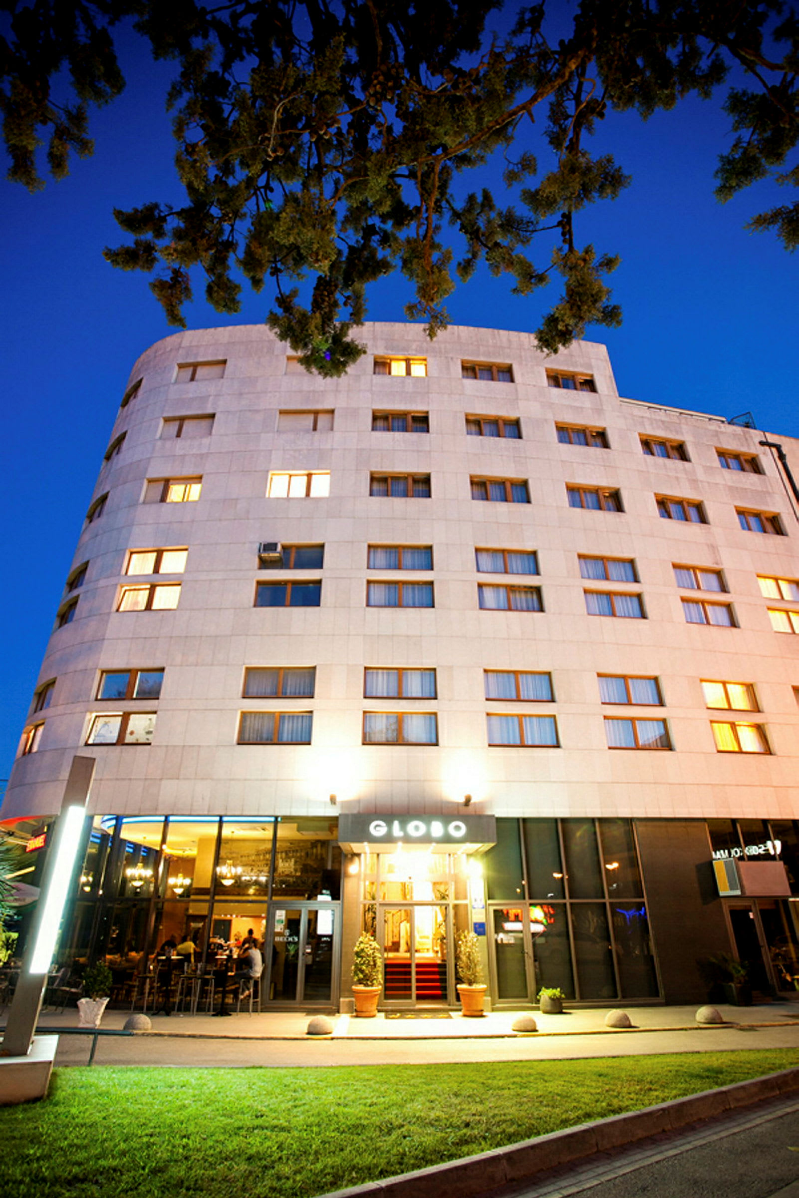 Et hotell med opplyst fasade og inngang, fotografert i skumringen. (AI-generert tekst)