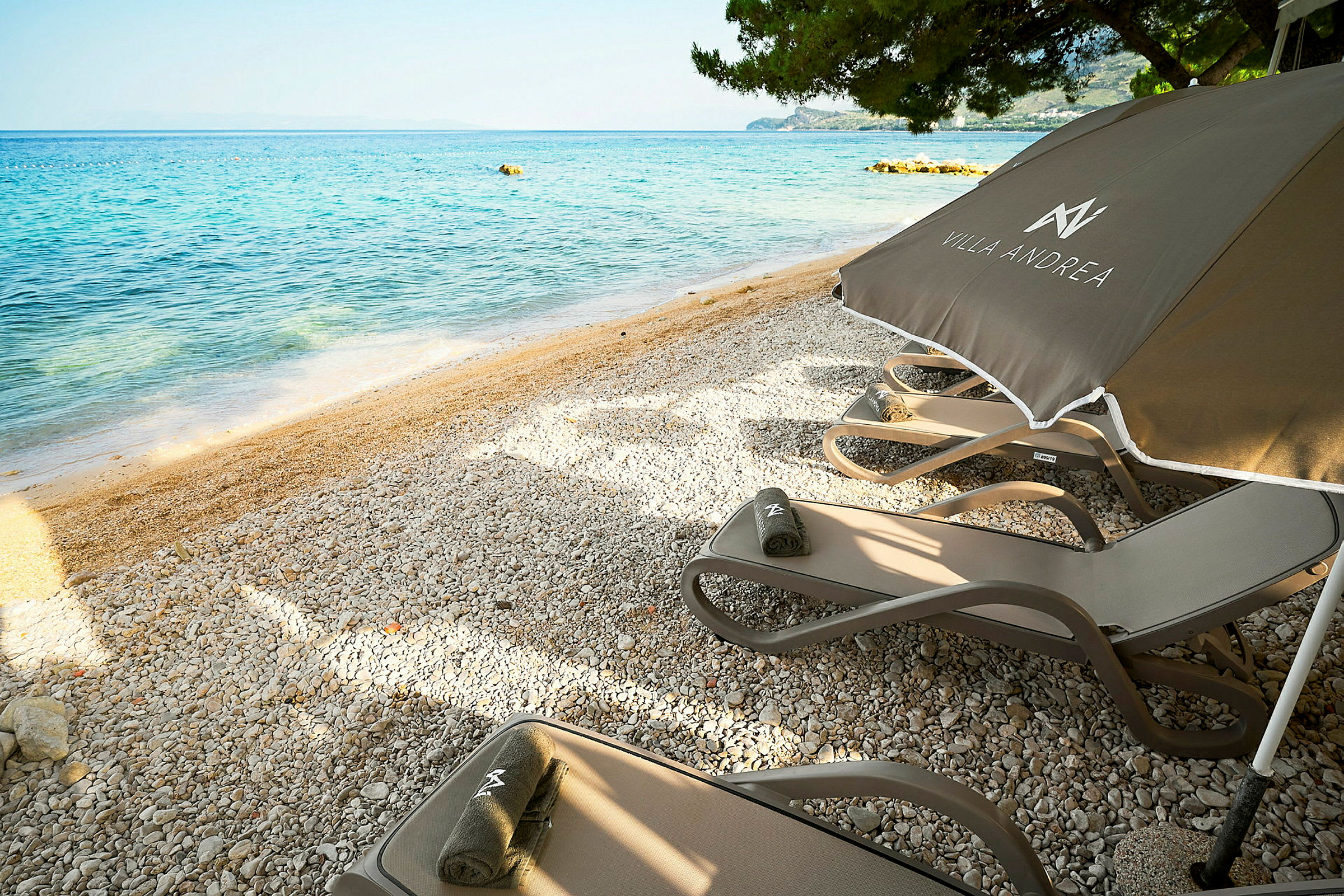 Solstoler og parasoller på en steinstrand med utsikt over havet. (AI-generert tekst)