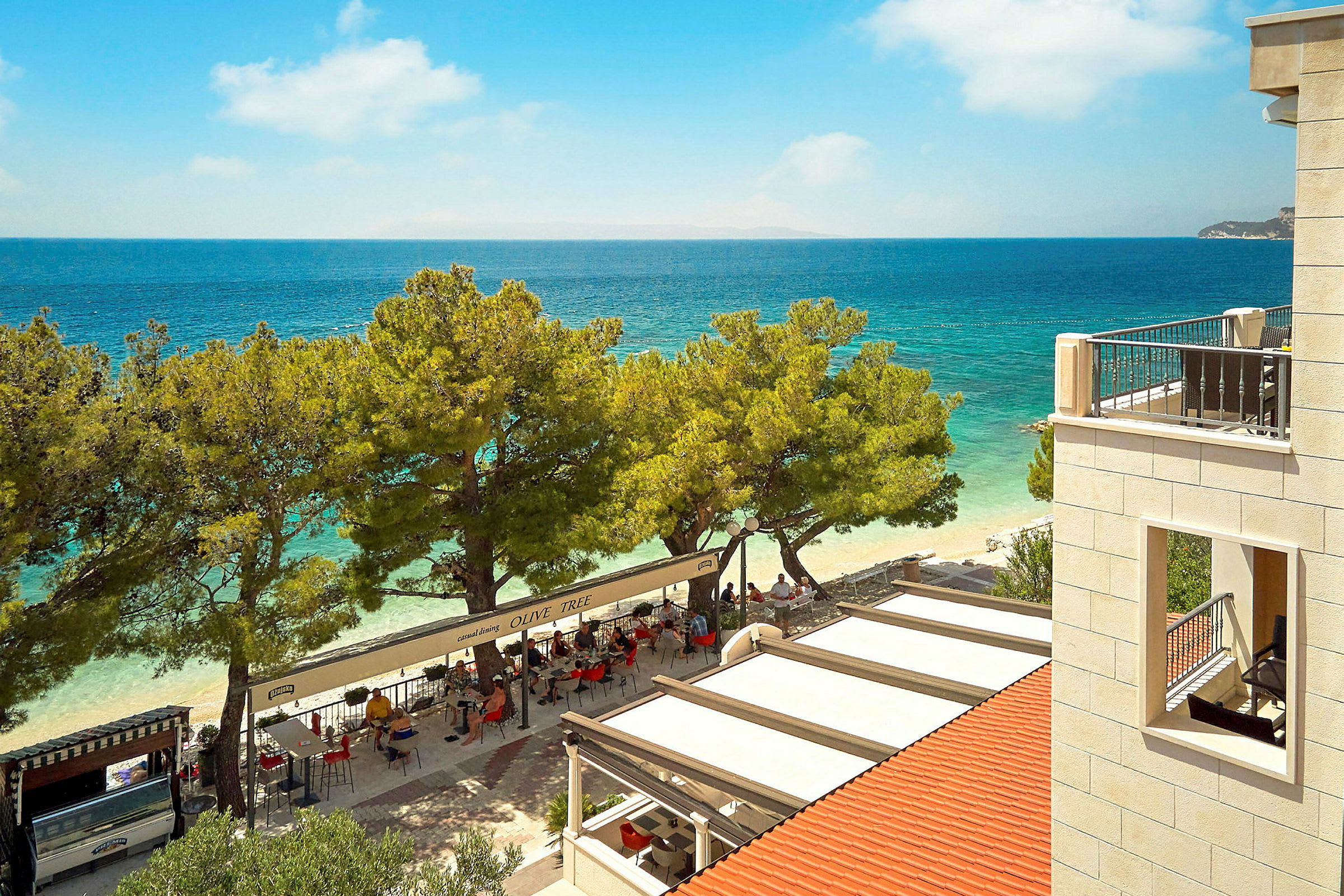 Utsikt over en restaurant ved stranden med havet i bakgrunnen. (AI-generert tekst)