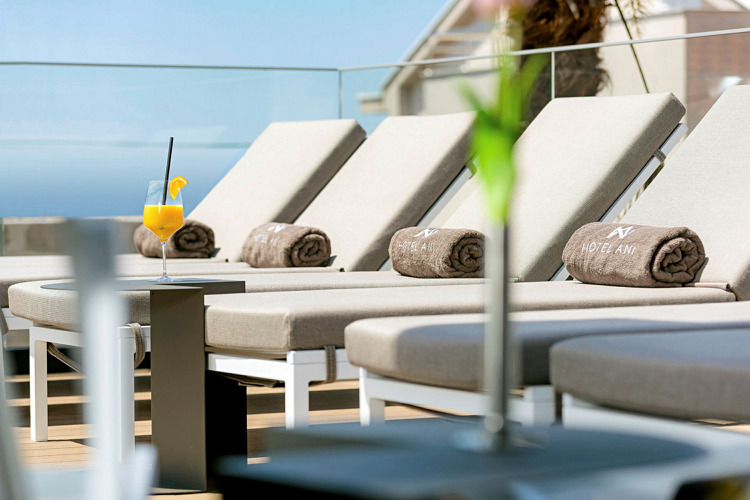 Solstoler med hotellhåndklær på en terrasse, et glass appelsinjuice står på et bord. (AI-generert tekst)