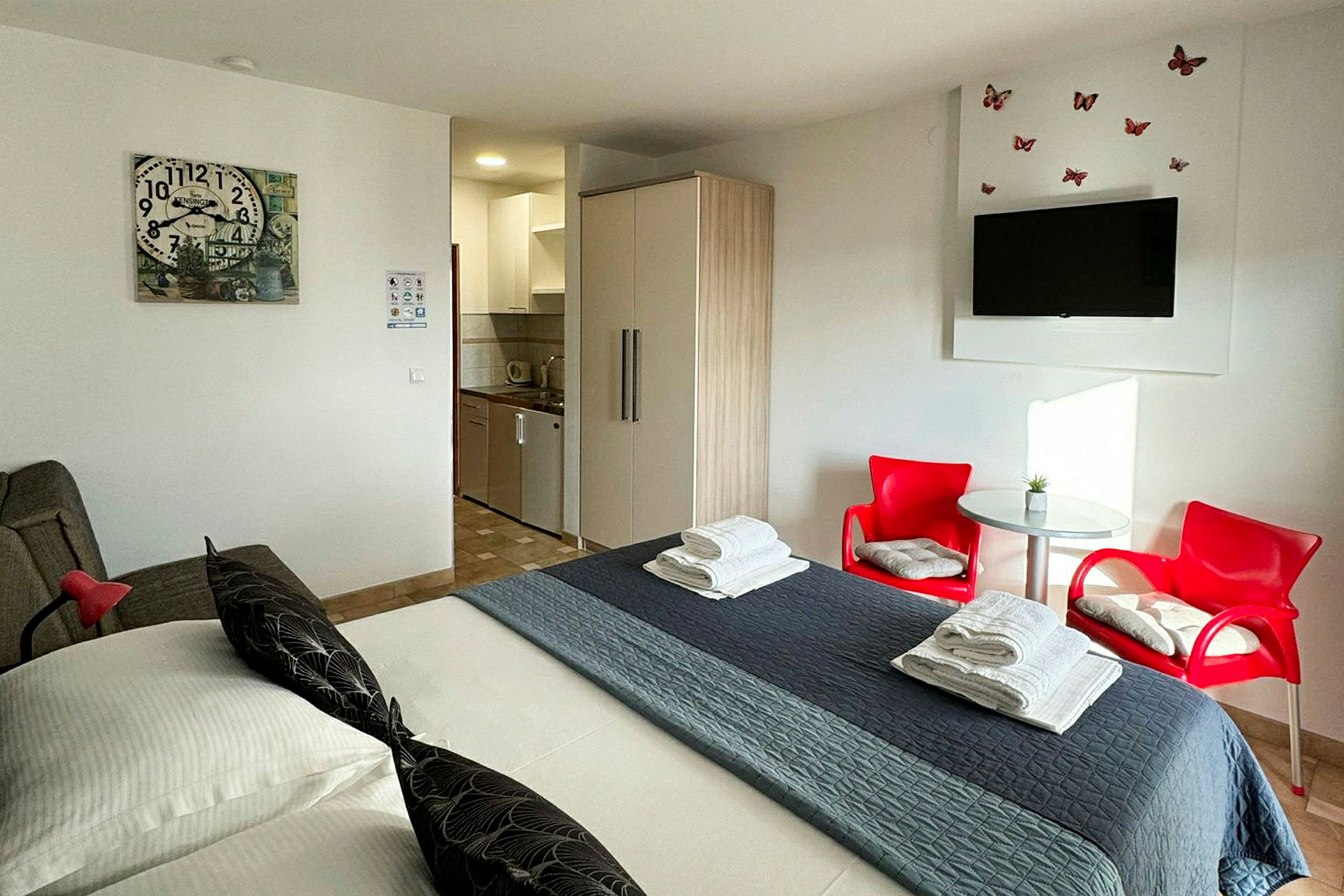 Et hotellrom med en seng, røde stoler, bord, garderobe og et lite kjøkken. (AI-generert tekst)