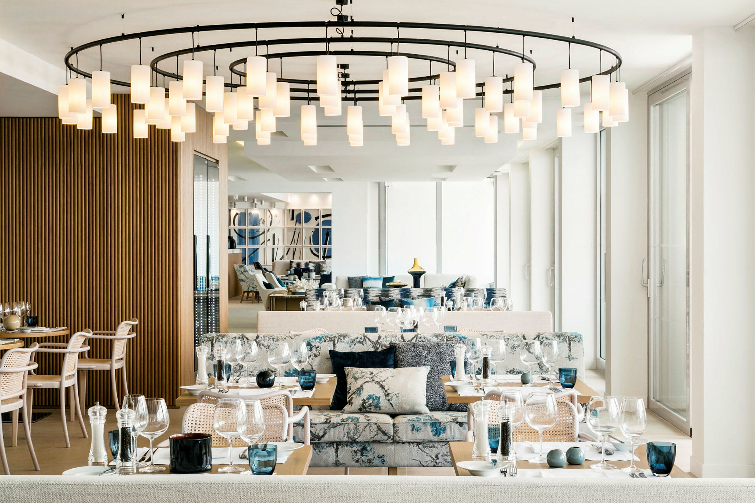 Interiør av en elegant restaurant med dekkede bord, moderne stoler og en hengende lysekrone i taket. (AI-generert tekst)