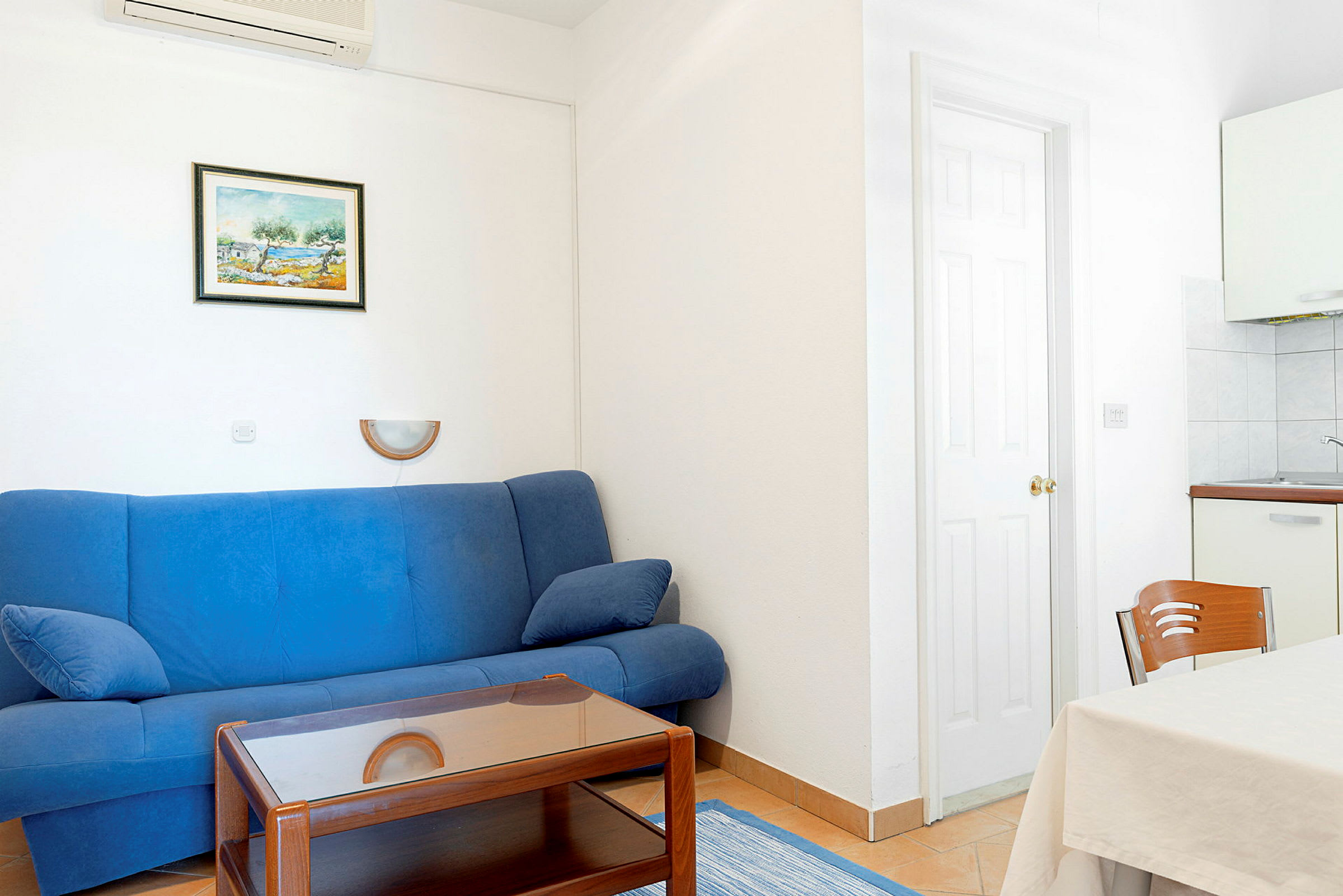 Stue med blå sofa, trebord, spisebord med hvit duk og veggdekorasjon. (AI-generert tekst)