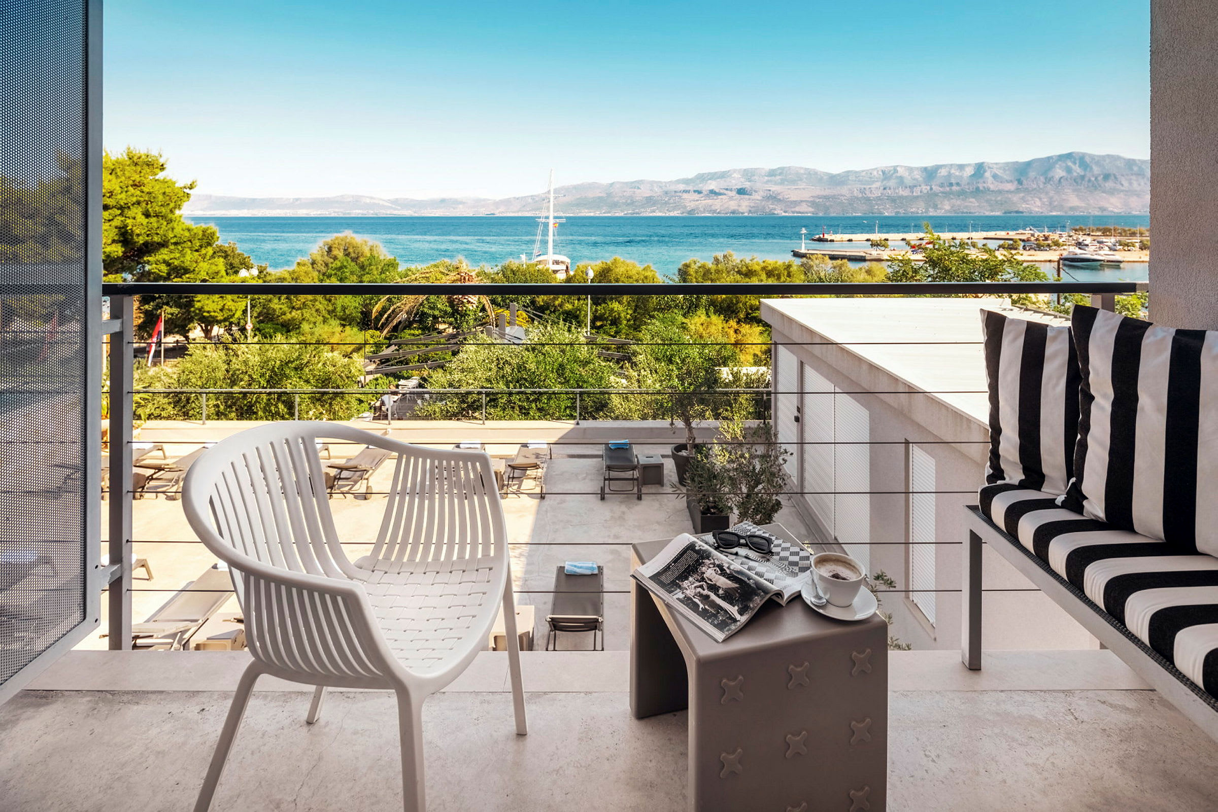 Utsikt fra en terrasse med møbler, utsikt mot havet og fjell. (AI-generert tekst)
