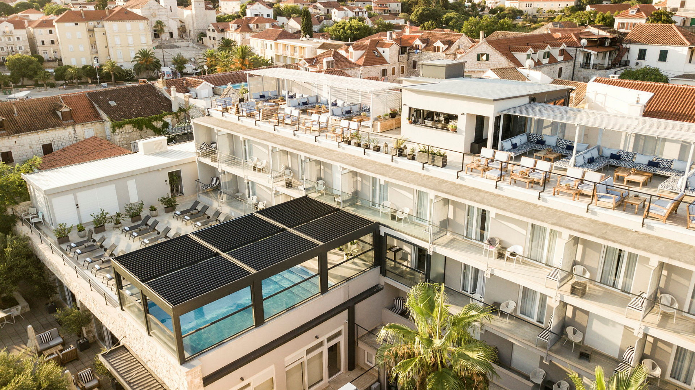 Hotellbygning med basseng, terrasse og omkringliggende hus. (AI-generert tekst)