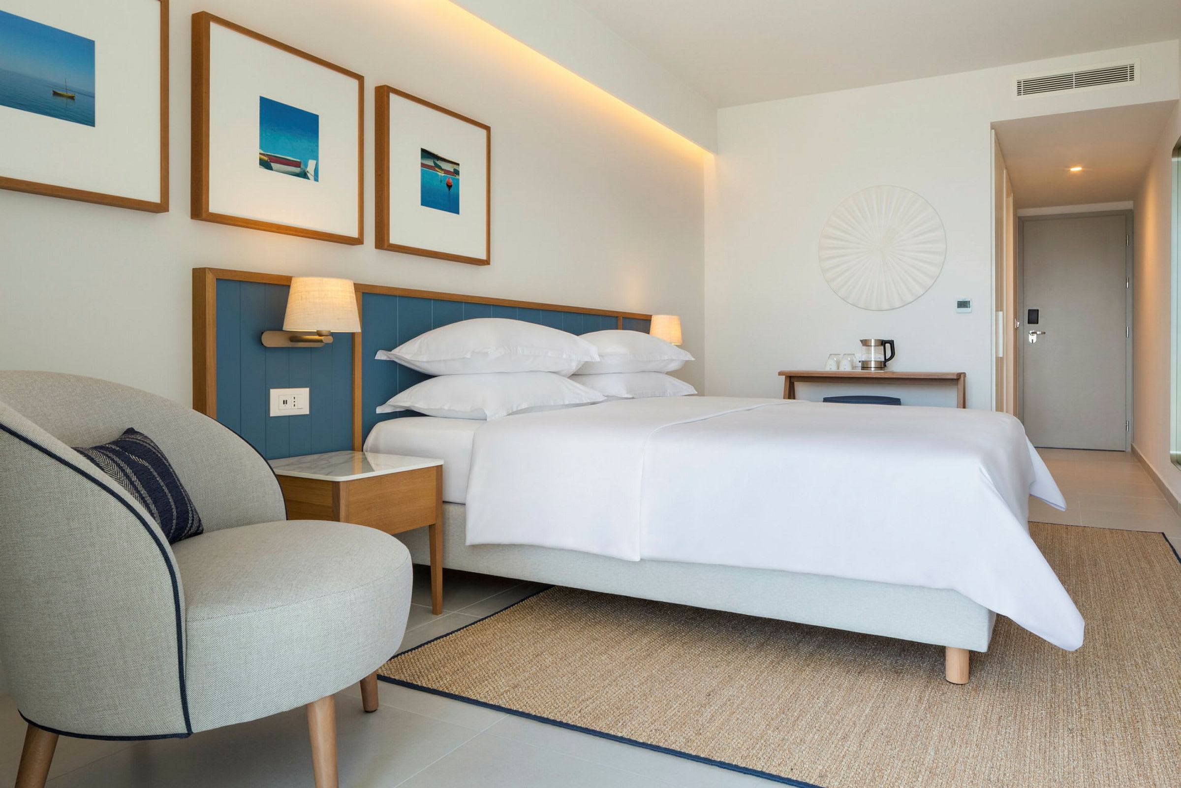 Et hotellrom med en seng, nattbord, en lenestol, en dør og dekorative veggdetaljer. (AI-generert tekst)