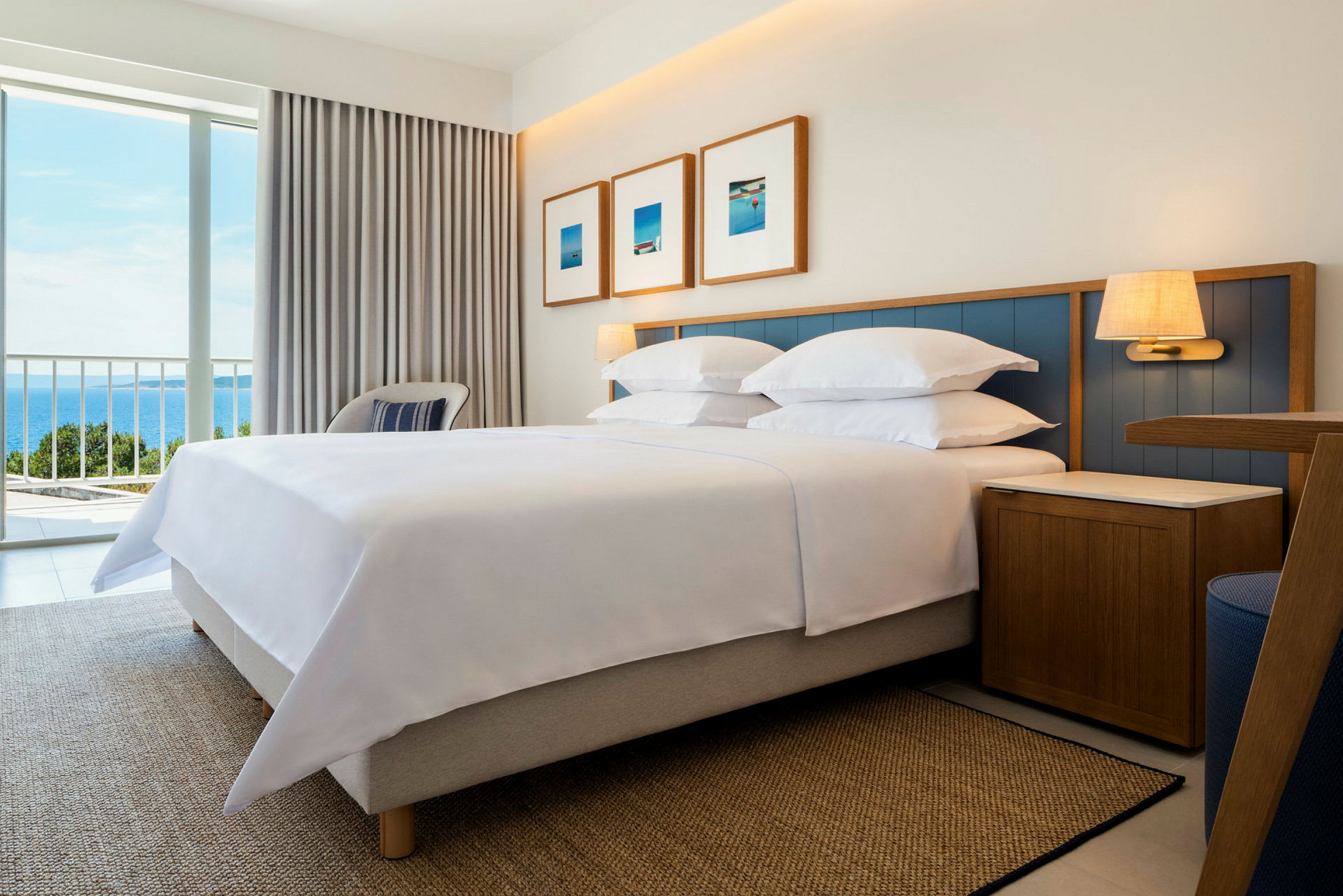 Hotellrom med seng, nattbord og vindu med utsikt mot havet. (AI-generert tekst)