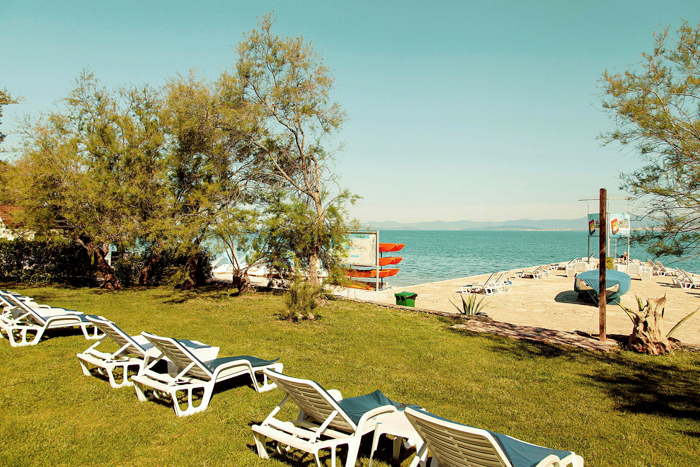 Gressplen med solsenger ved stranden og havet. (AI-generert tekst)