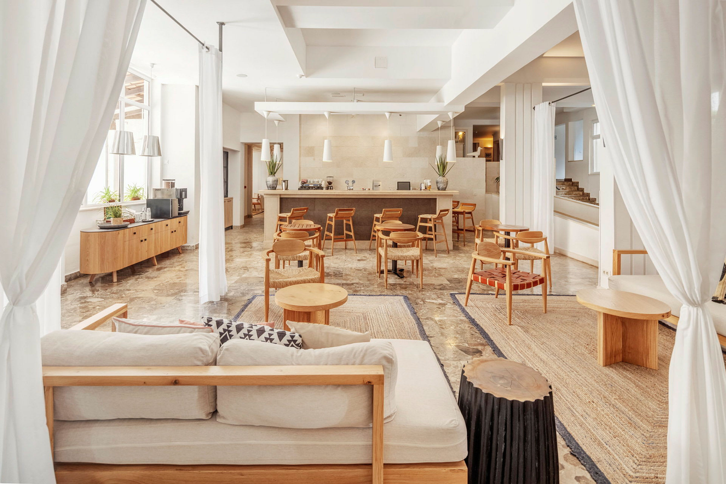 Lyst og romslig loungeområde med sofaer, små trebord og en bardisk i bakgrunnen. (AI-generert tekst)
