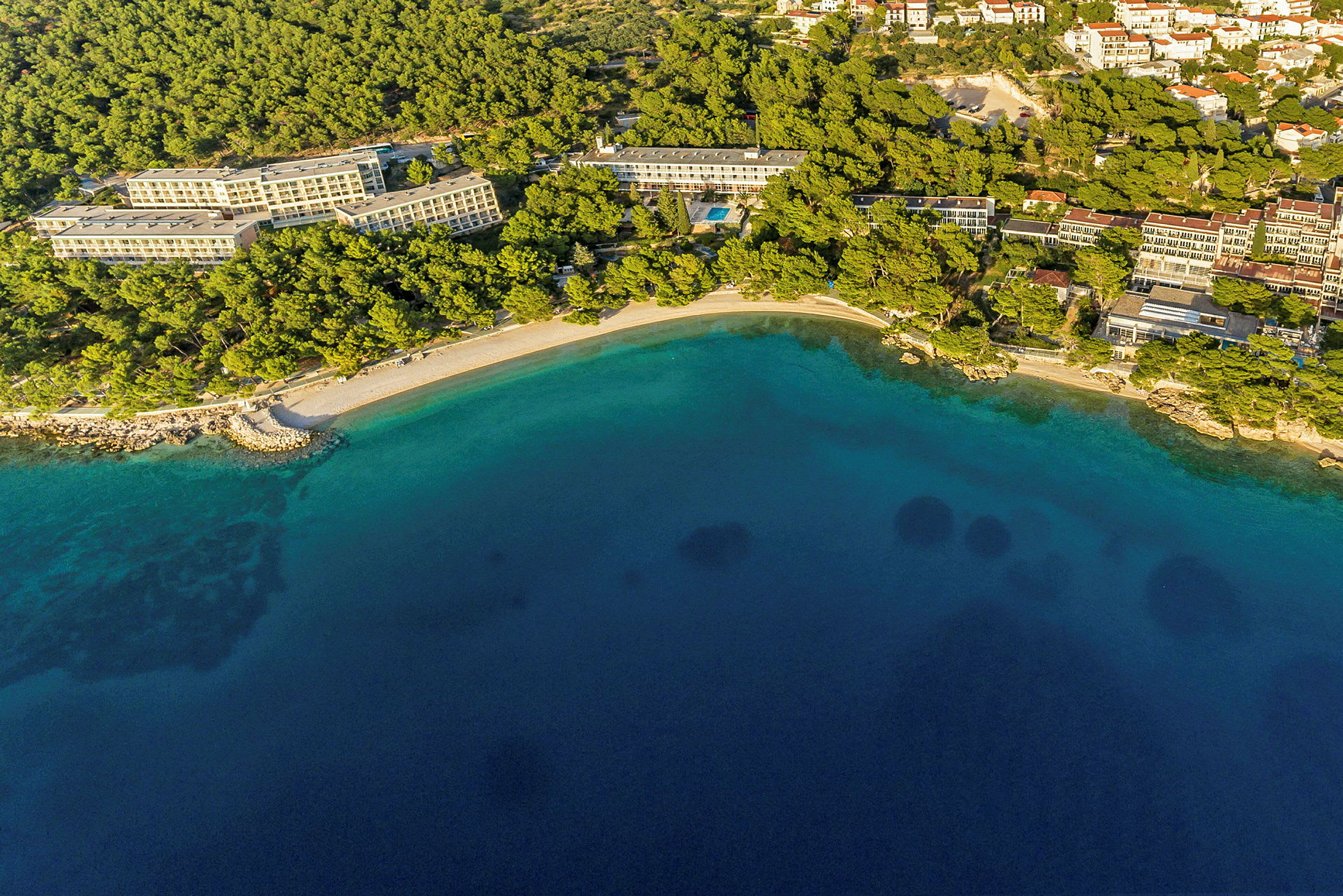 Flyfoto av hotell ved kysten med strand og klart vann. (AI-generert tekst)