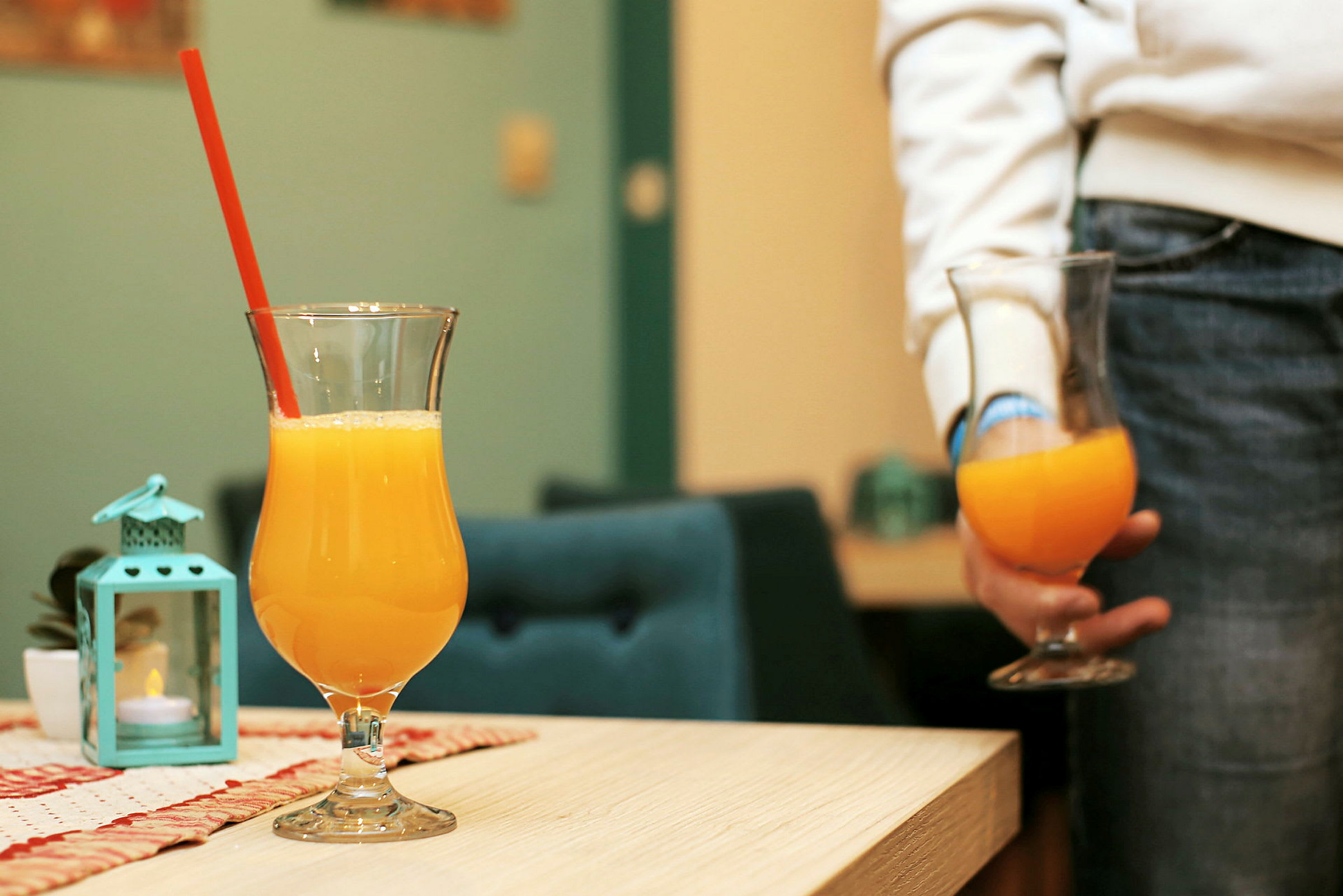 To glass med appelsinjuice, ett på et bord og ett holdes i hånden. (AI-generert tekst)
