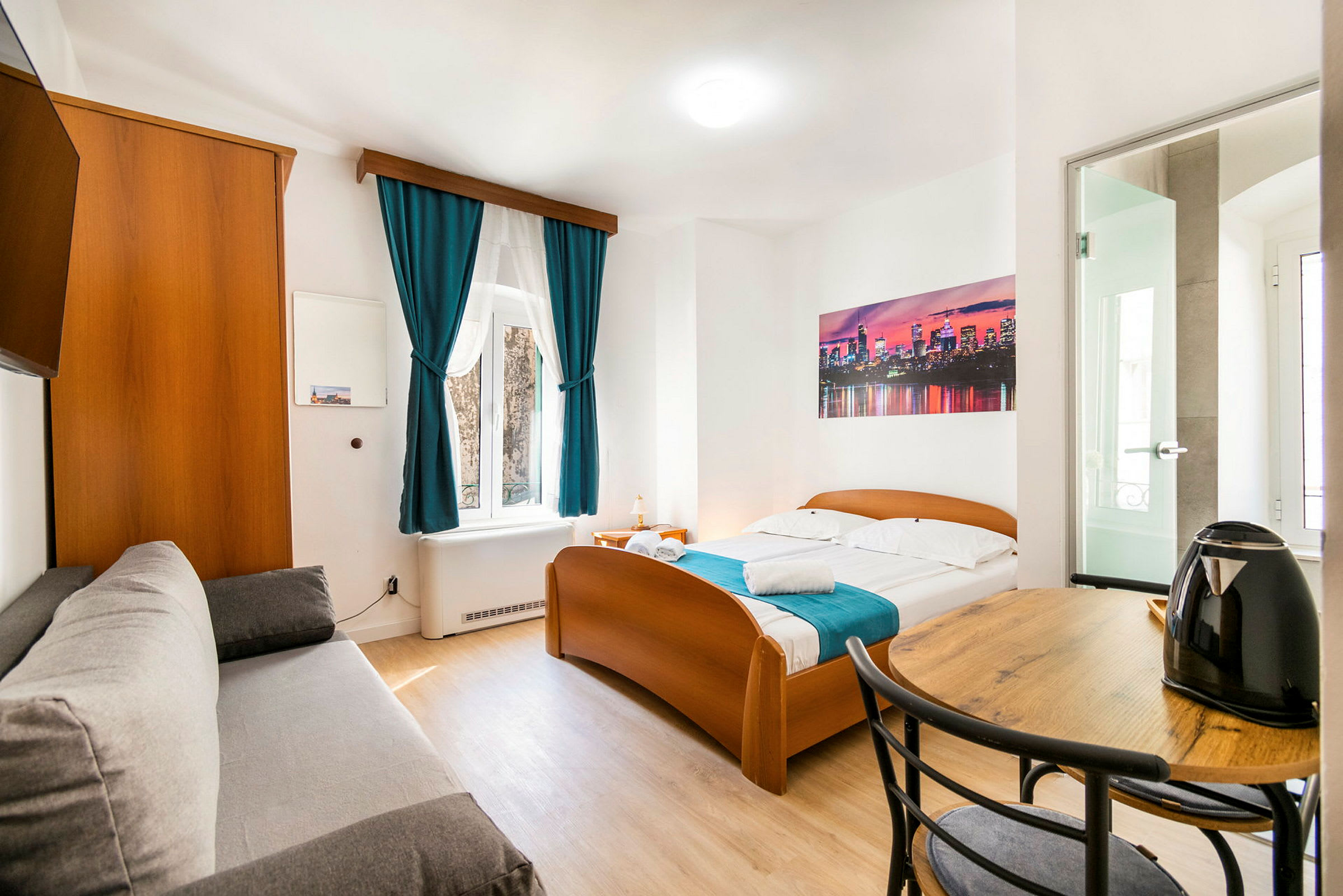 Bilde av et lyst hotellrom med seng, sofa, bord og en vannkoker. (AI-generert tekst)