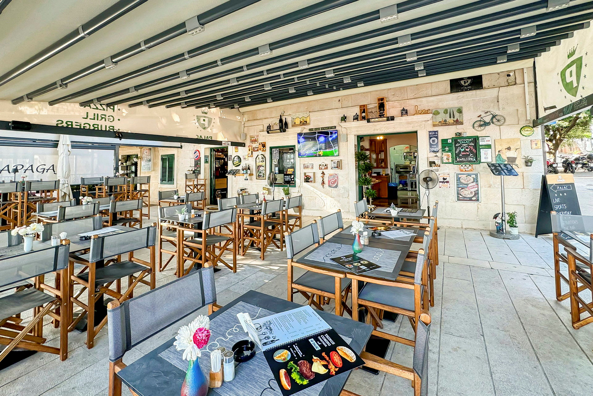Restaurant med uteservering, bord og stoler, samt dekorasjoner og en TV på veggen. (AI-generert tekst)