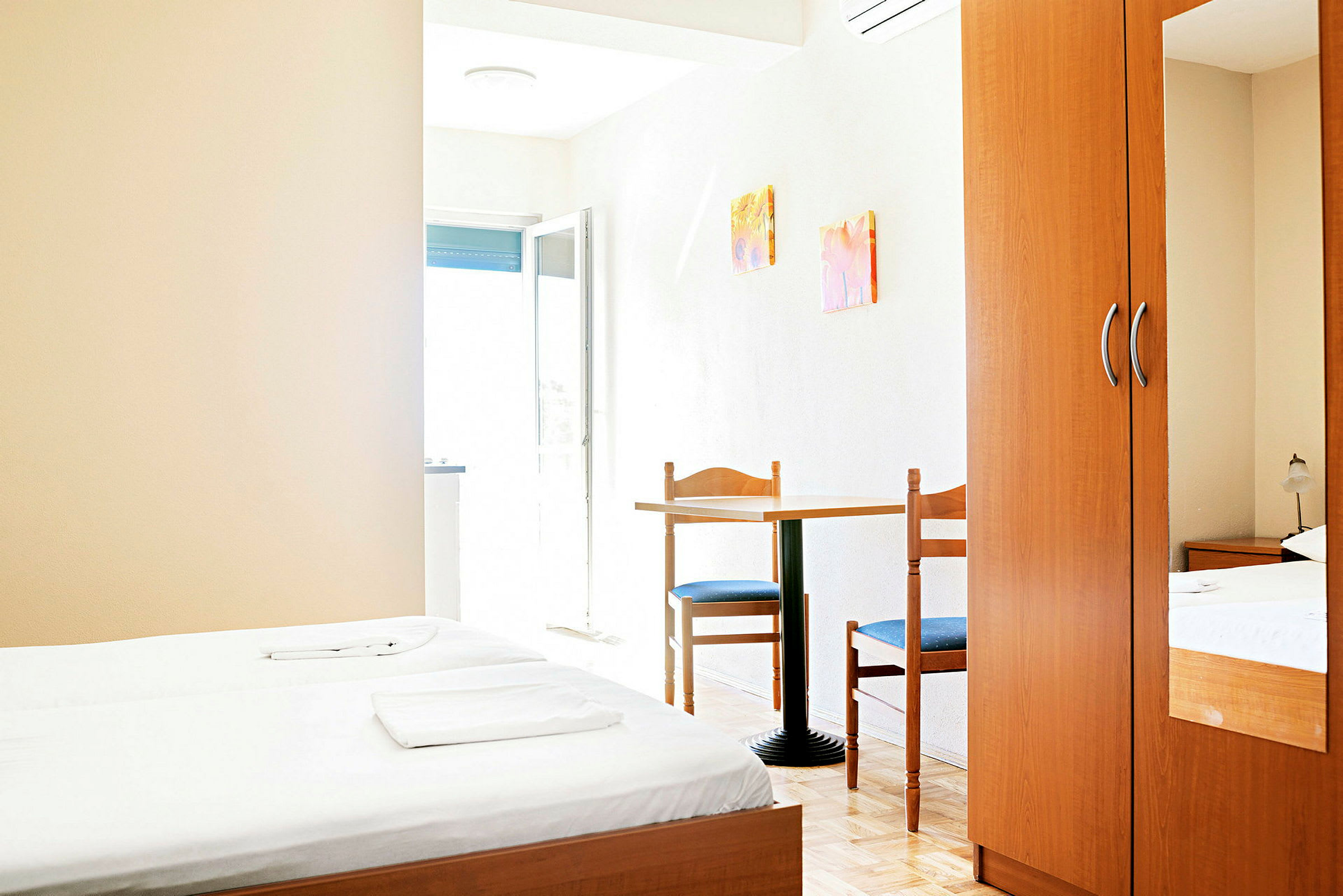 Et hotellrom med to enkeltsenger, et bord med to stoler og en garderobe. (AI-generert tekst)