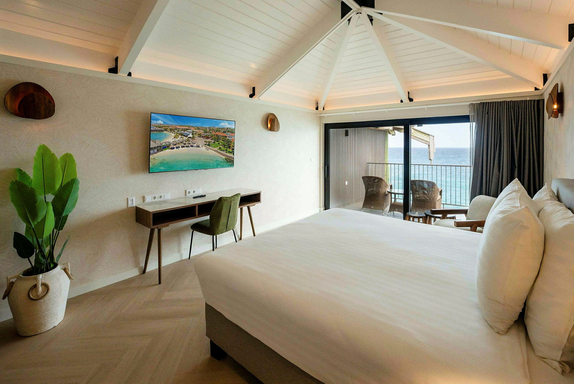Et hotellrom med en dobbeltseng, skrivebord, TV og balkong med utsikt over havet. (AI-generert tekst)