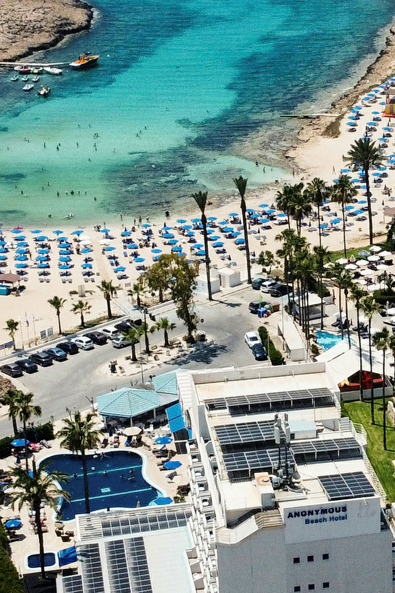 Hotell med basseng og nærliggende strand fylt med solsenger og parasoller ved et turkis hav. (AI-generert tekst)