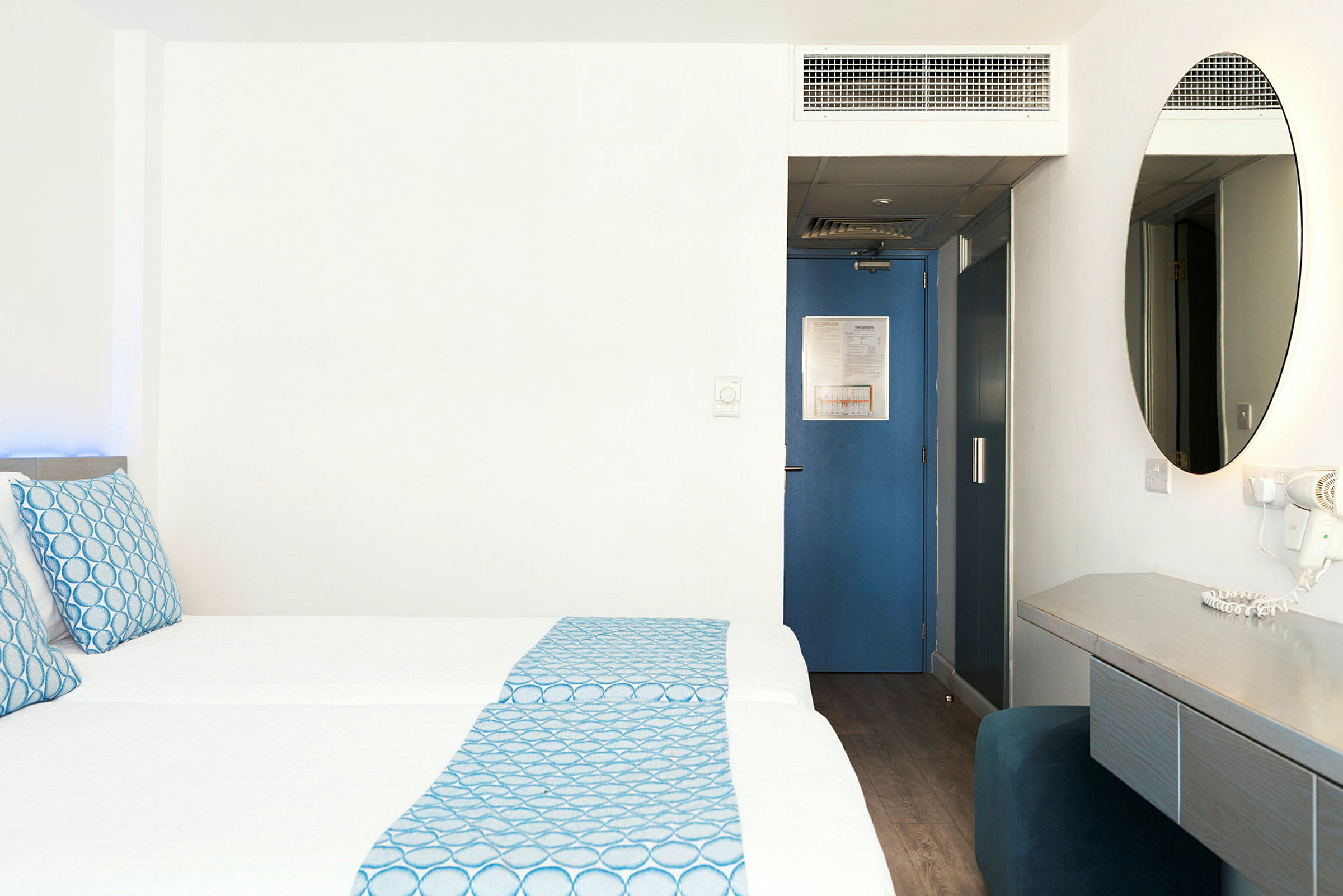 Hotellrom med to senger, blå detaljer og skrivebord. (AI-generert tekst)