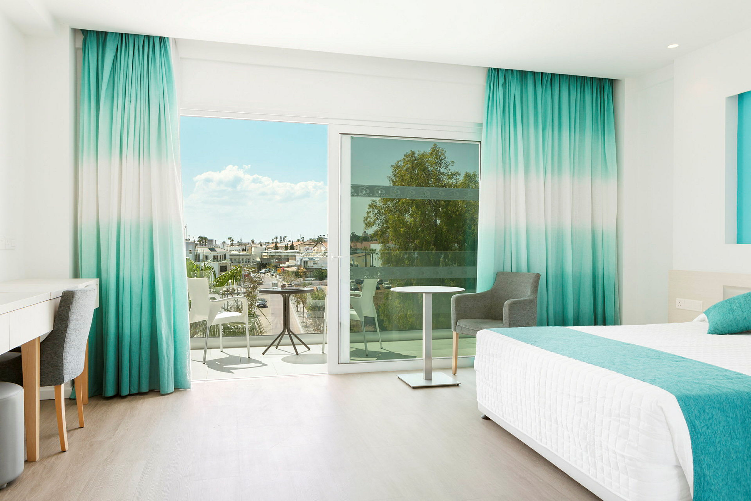 Hotellrom med havutsikt gjennom store vinduer og balkong. (AI-generert tekst)