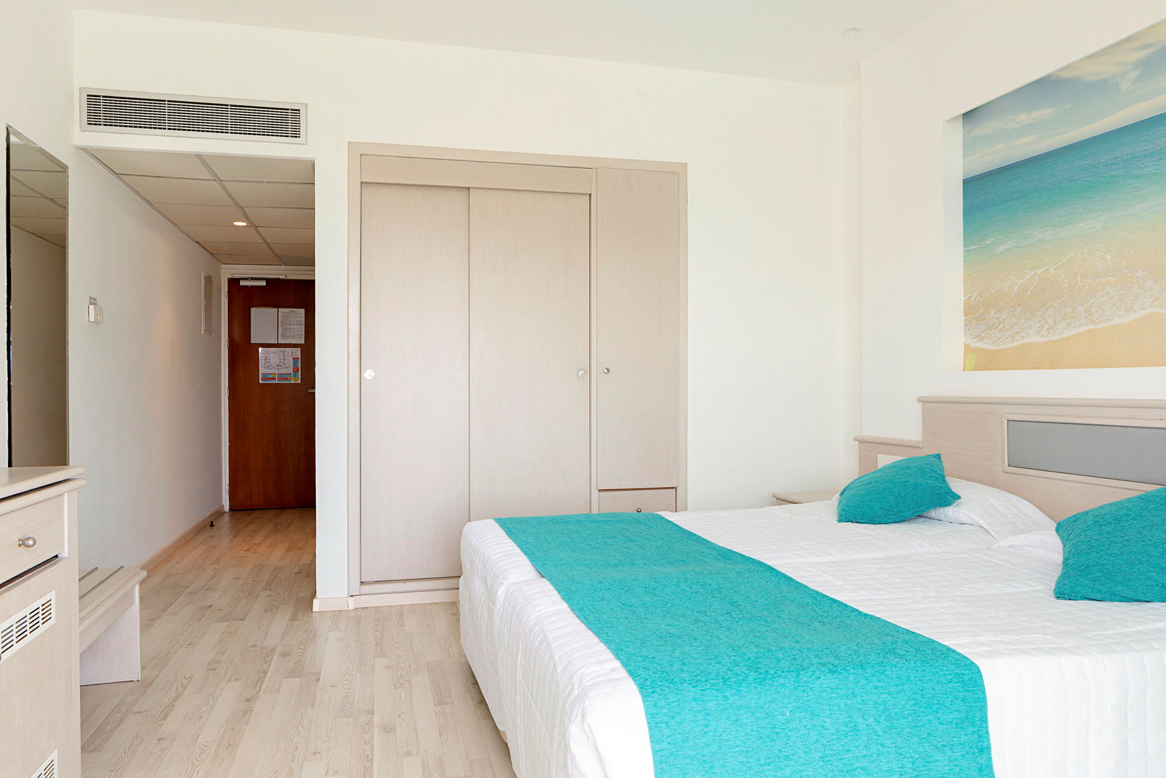 Hotellrom med dobbeltseng og blått sengeteppe. (AI-generert tekst)