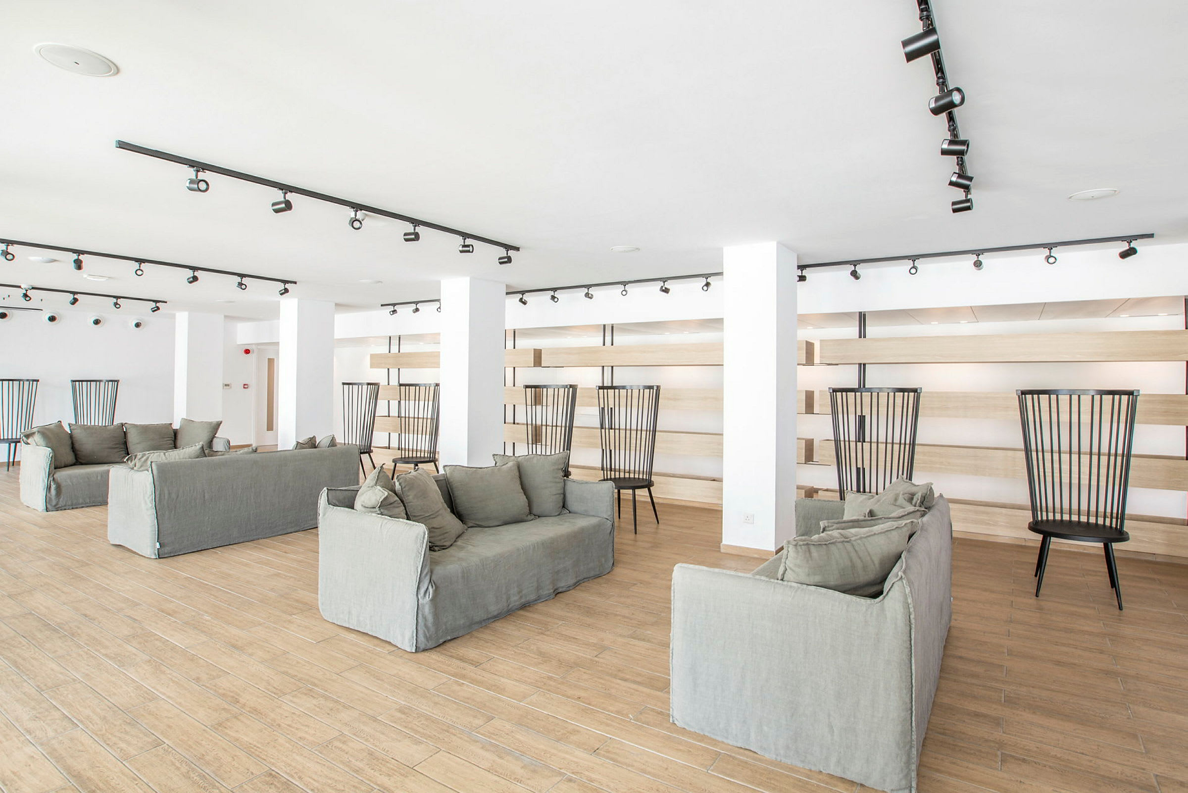 Et lyst rom med flere sofaer og stoler, gulvet er laget av tre, og rommet er innredet med moderne design. (AI-generert tekst)