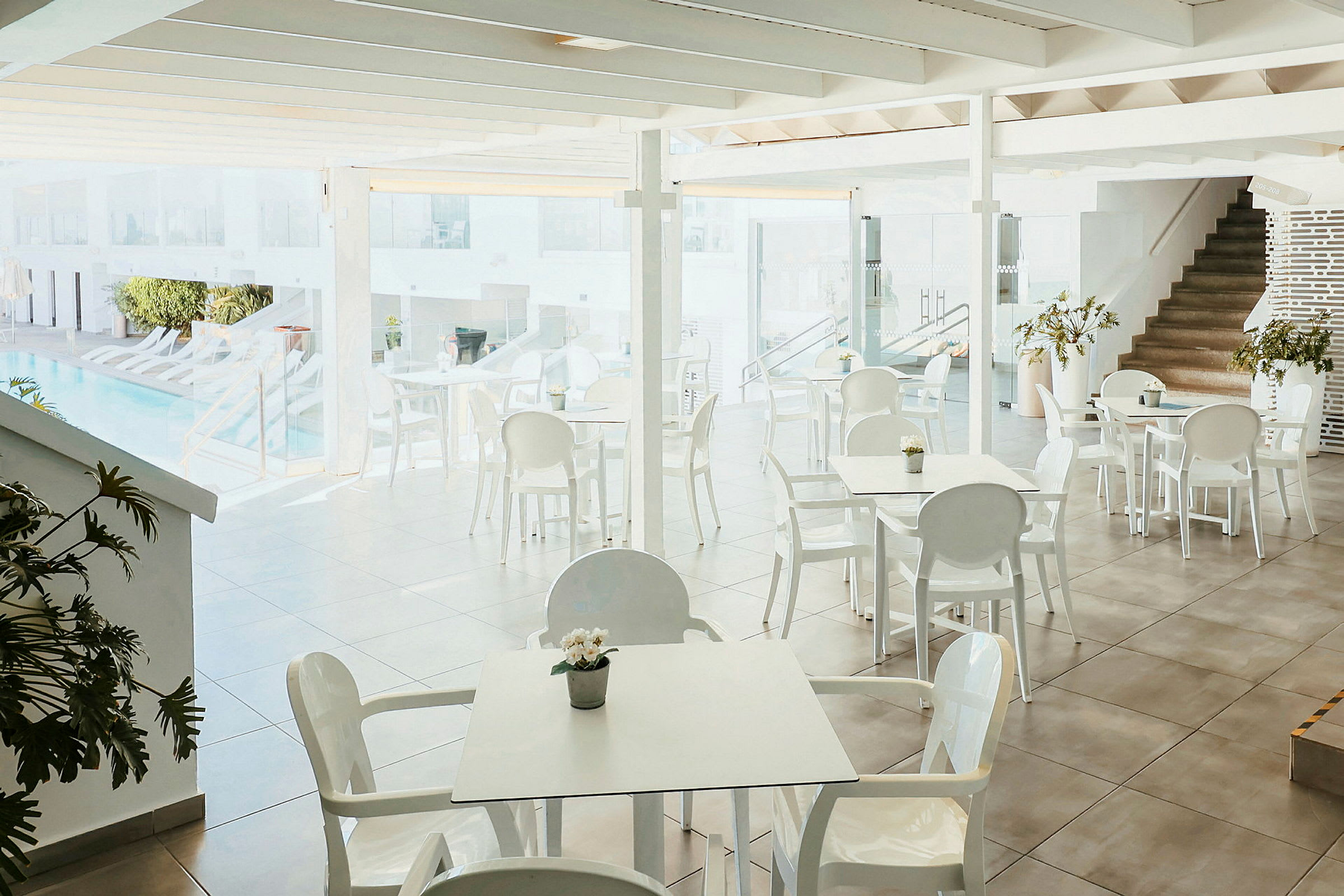 En lys restaurant med hvite bord og stoler ved siden av et basseng. (AI-generert tekst)