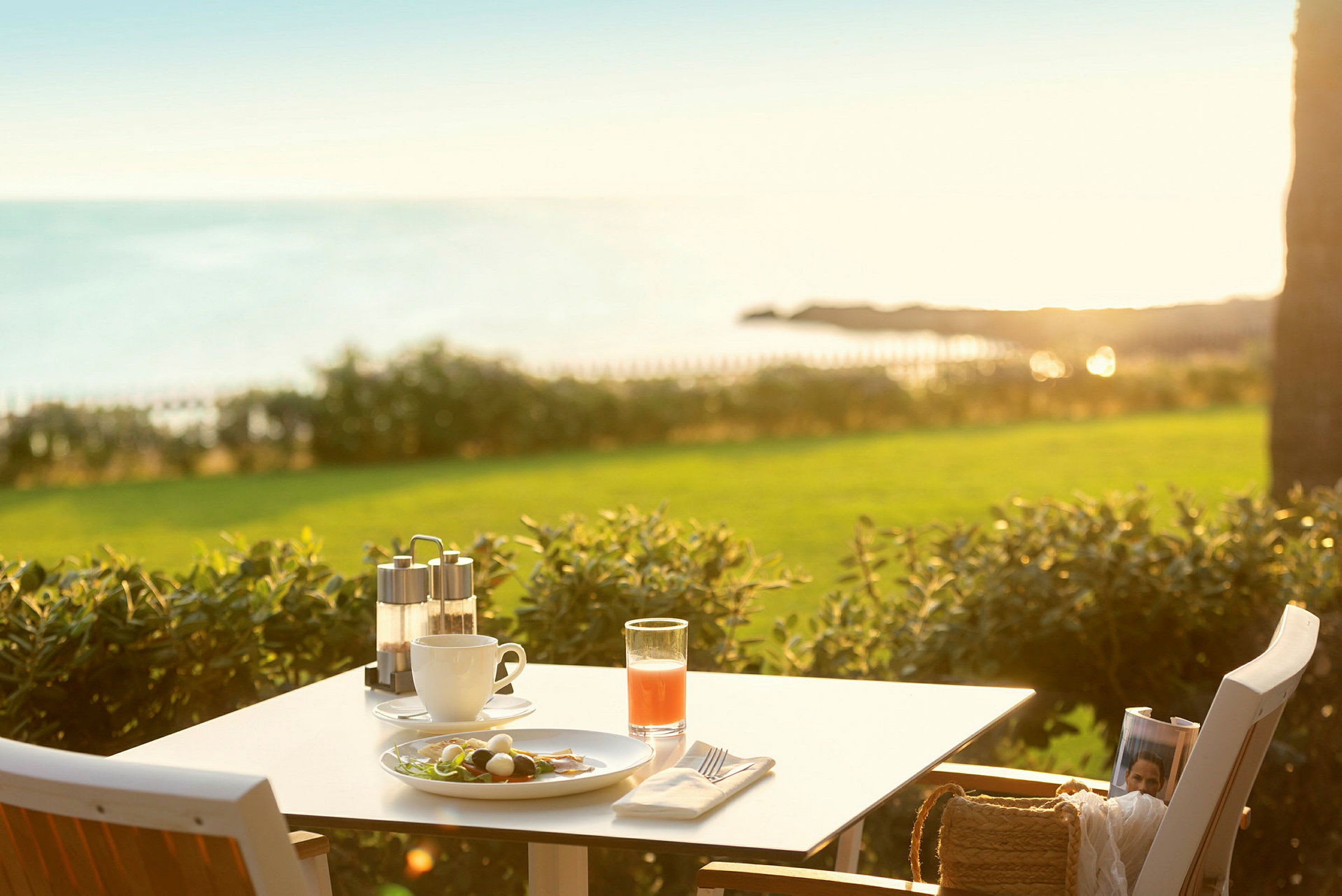 Et bord med frokost med utsikt over havet og det grønne området i solen. (AI-generert tekst)