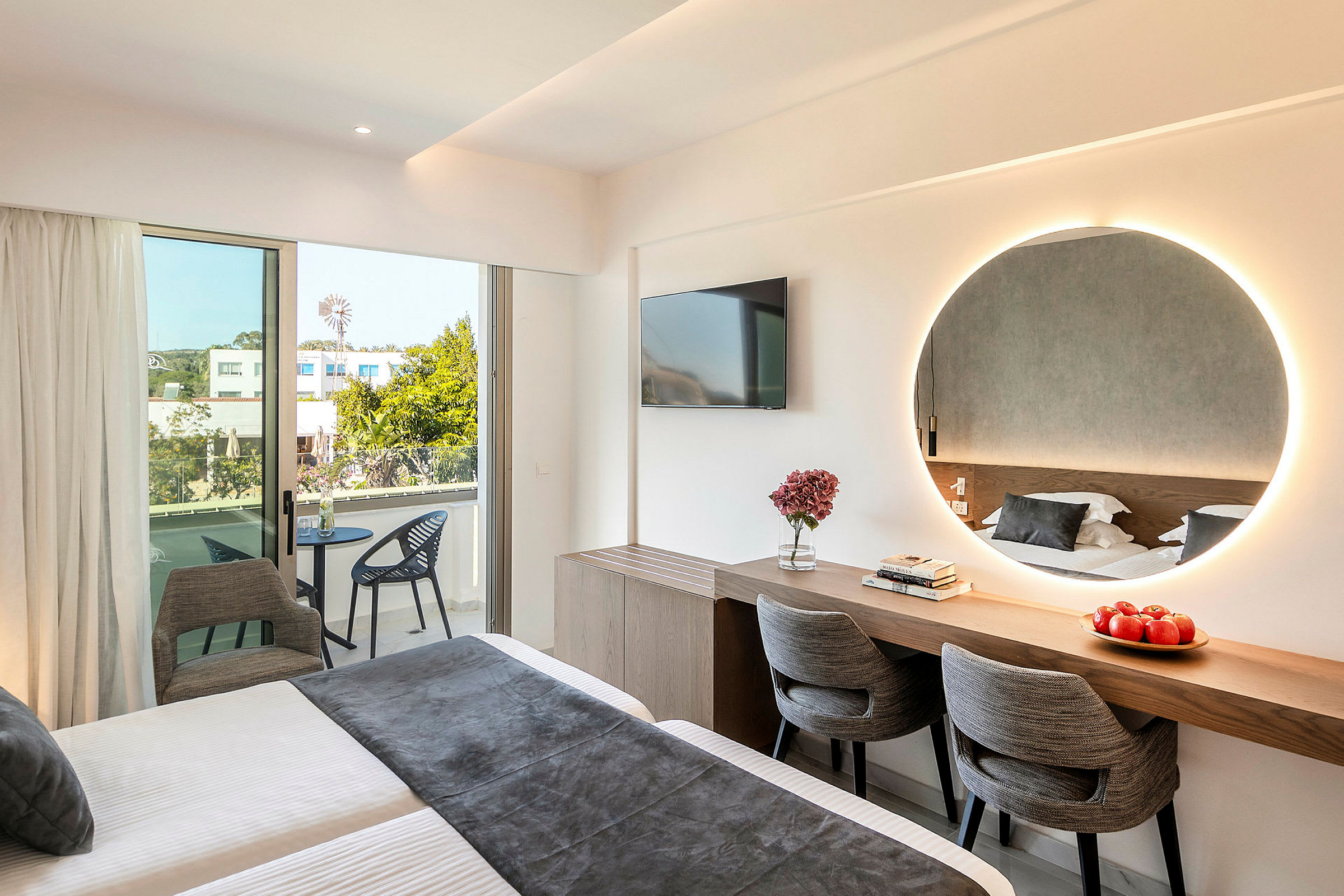 Moderne hotellrom med seng, speil, skrivebord, stoler og balkong. (AI-generert tekst)