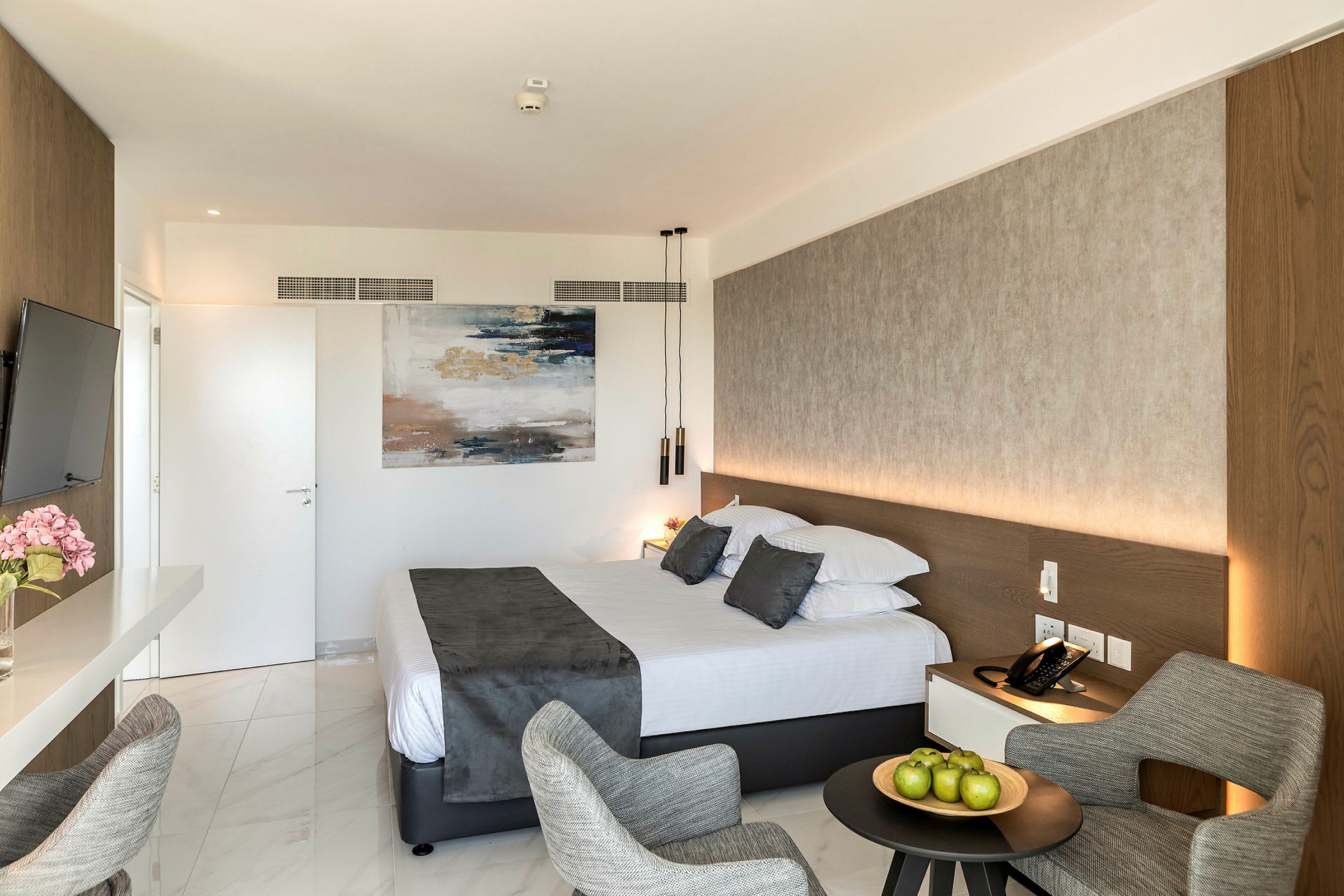 Hotellrom med en dobbeltseng, en sittegruppe og kunst på veggen. (AI-generert tekst)