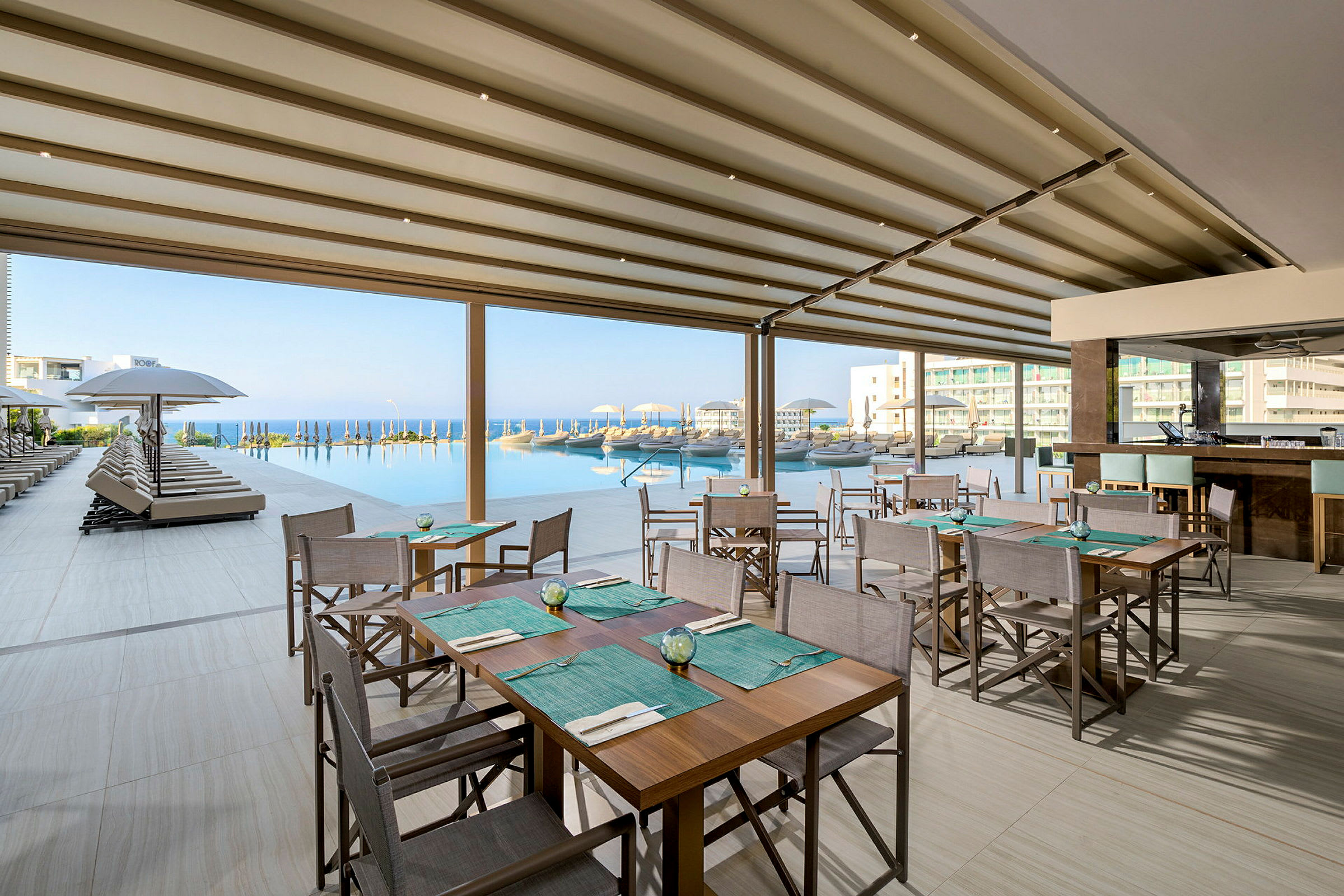 Restaurant med sitteplasser ved et basseng med utsikt over havet. (AI-generert tekst)