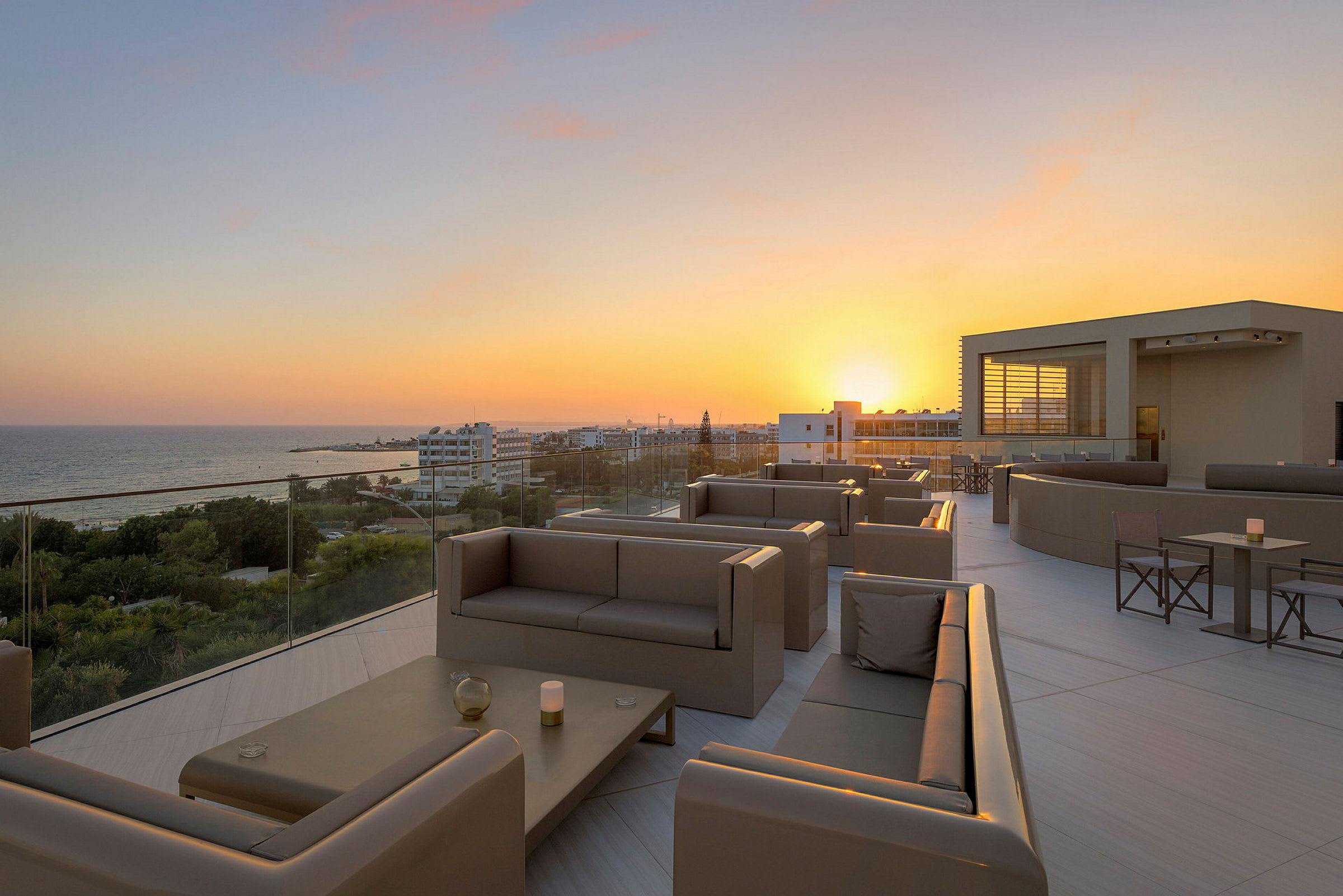 Terrasse med sitteplasser og utsikt over solnedgang og hav. (AI-generert tekst)
