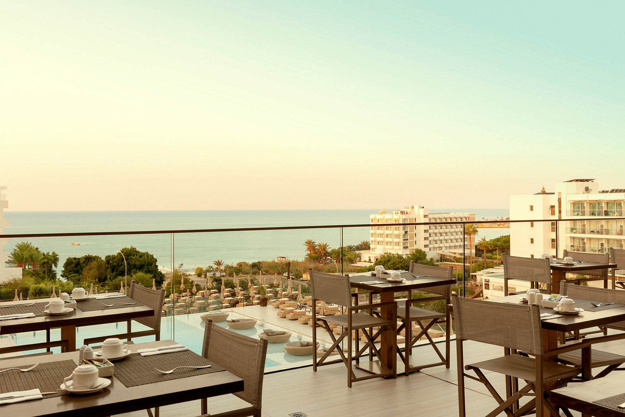 Restaurantterrasse med utsikt over havet og omgivende bygninger. (AI-generert tekst)