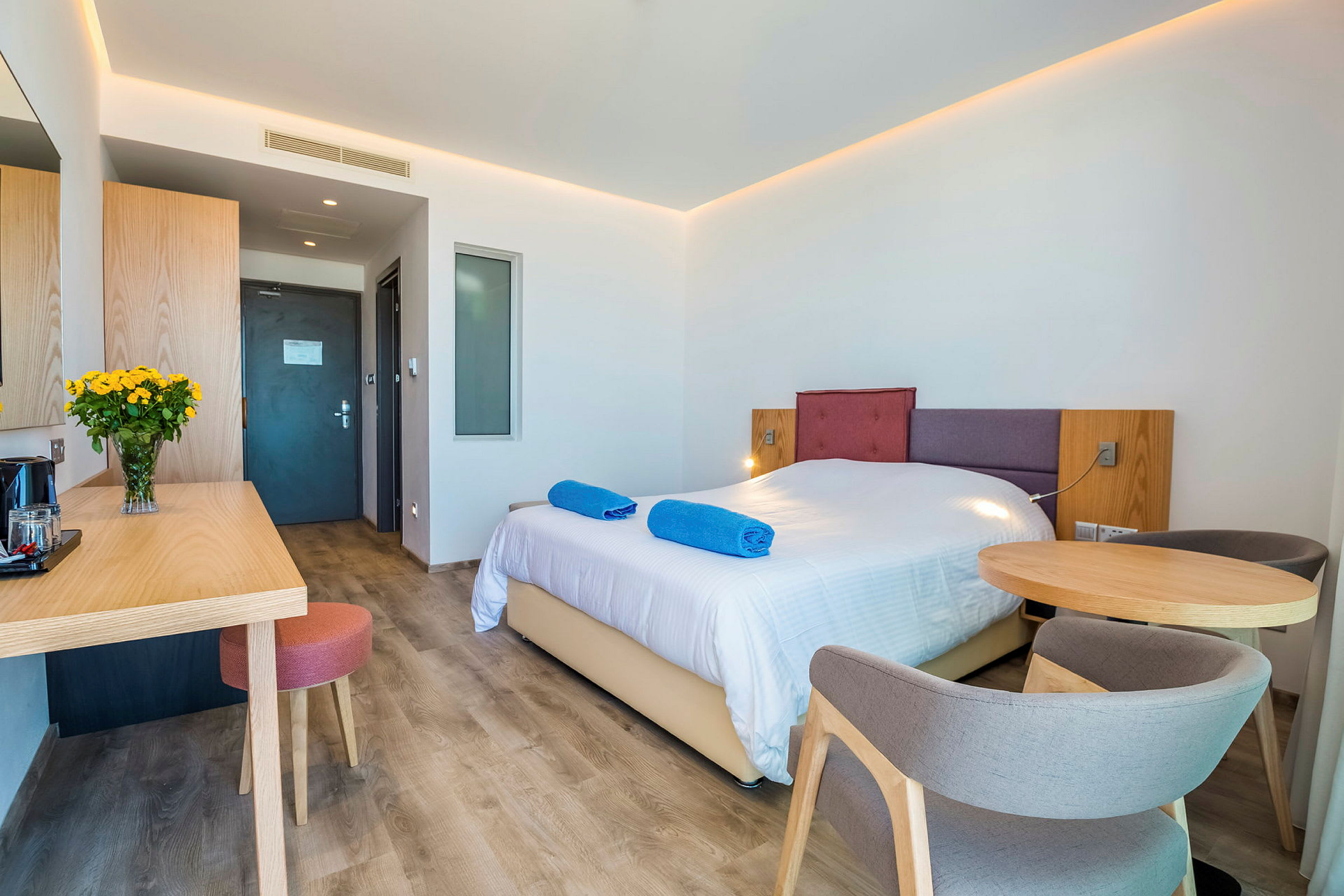 Hotellrom med en dobbeltseng, et bord med stoler og en skrivebordsoverflate. (AI-generert tekst)