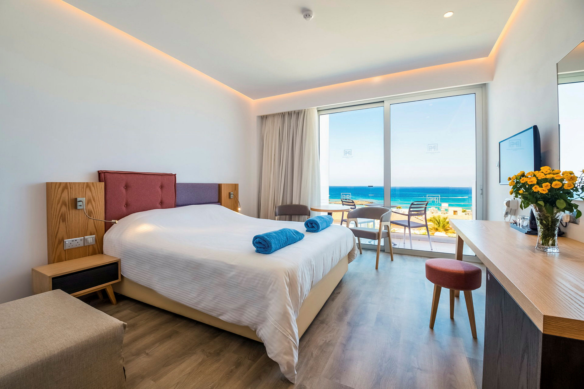 Hotellrom med en dobbeltseng, sittegruppe og utsikt over havet. (AI-generert tekst)