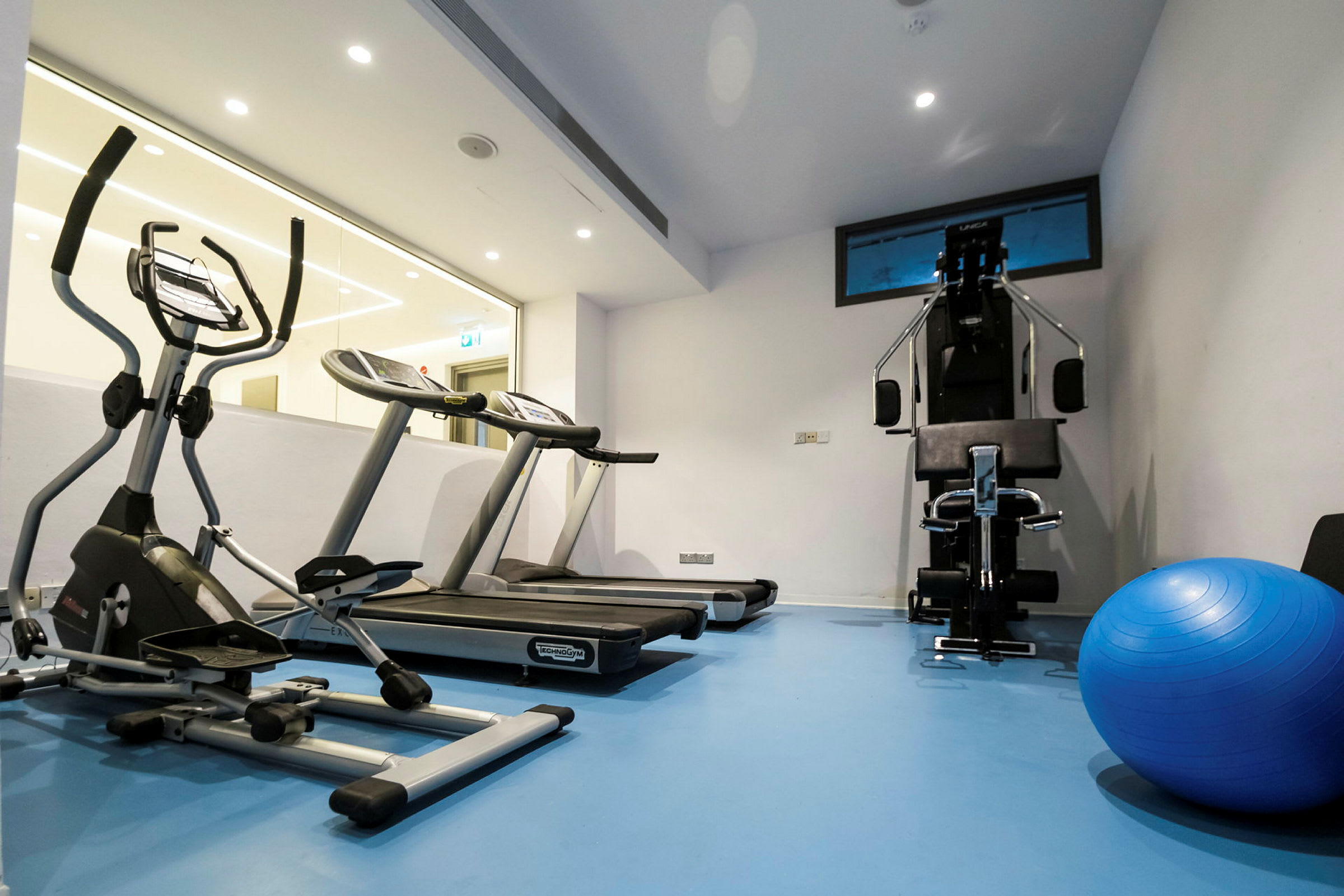 Et treningsrom med treningsmaskiner og en blå pilatesball. (AI-generert tekst)