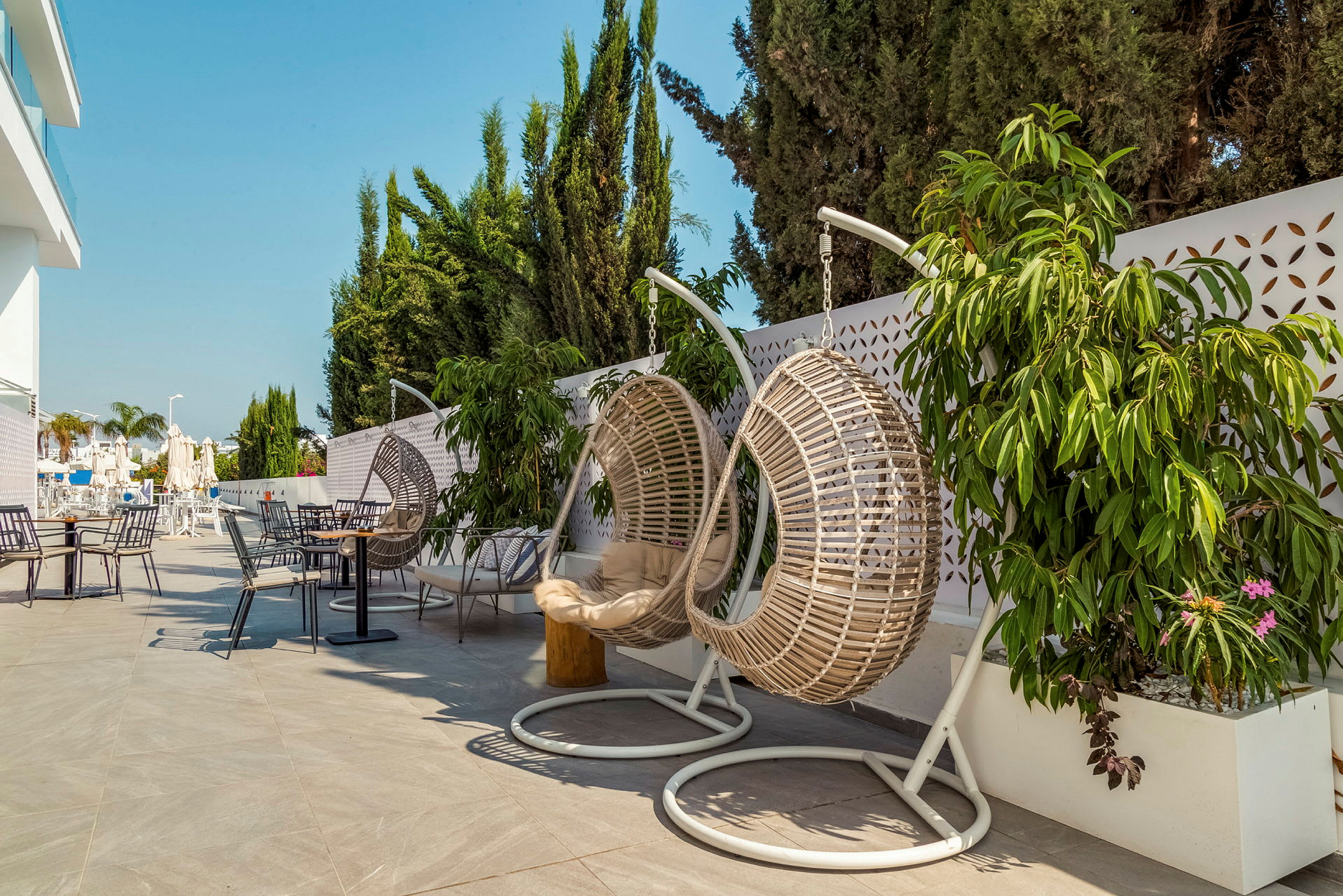 Hengende kurvstoler og bord på en terrasse med planter og parasoller. (AI-generert tekst)