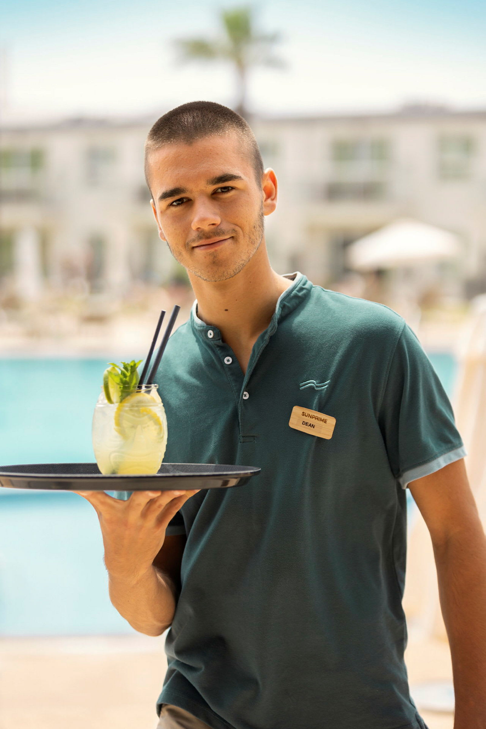 En person i uniform som bærer et serveringsbrett med en drink ved et basseng. (AI-generert tekst)