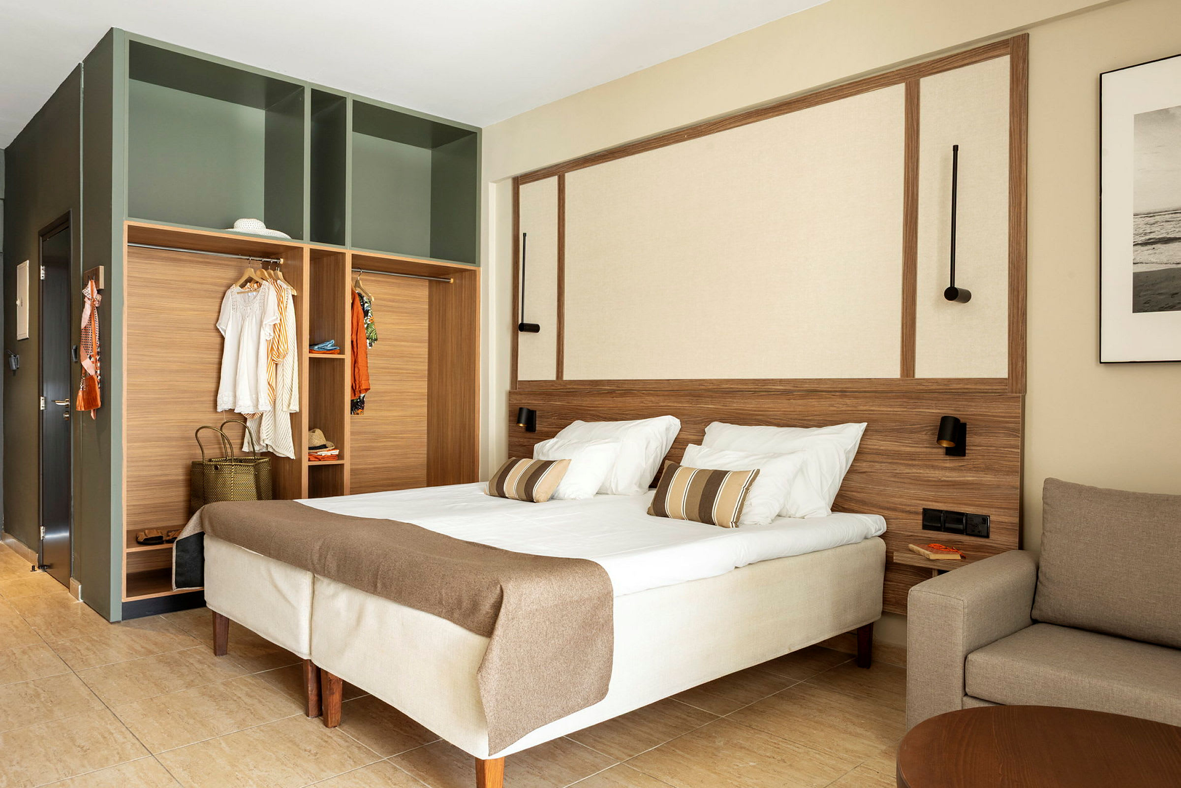 Et hotellrom med dobbeltseng, åpen garderobe og en sofa. (AI-generert tekst)